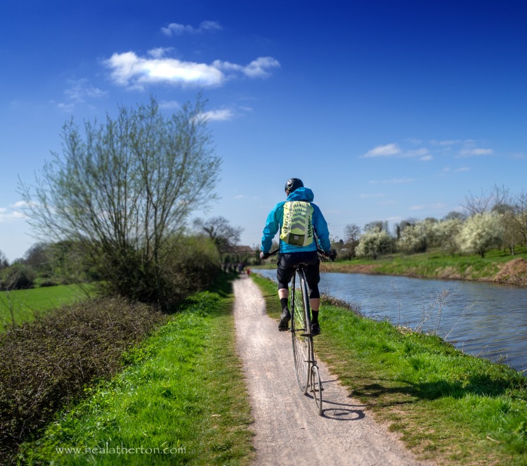 penny farthing bicycle on canal bank path with rider and canal by trees