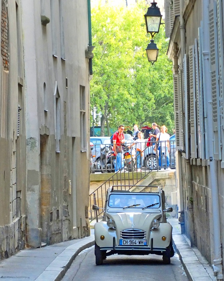 small car between narrow ancient buildings with people watching in Paris France