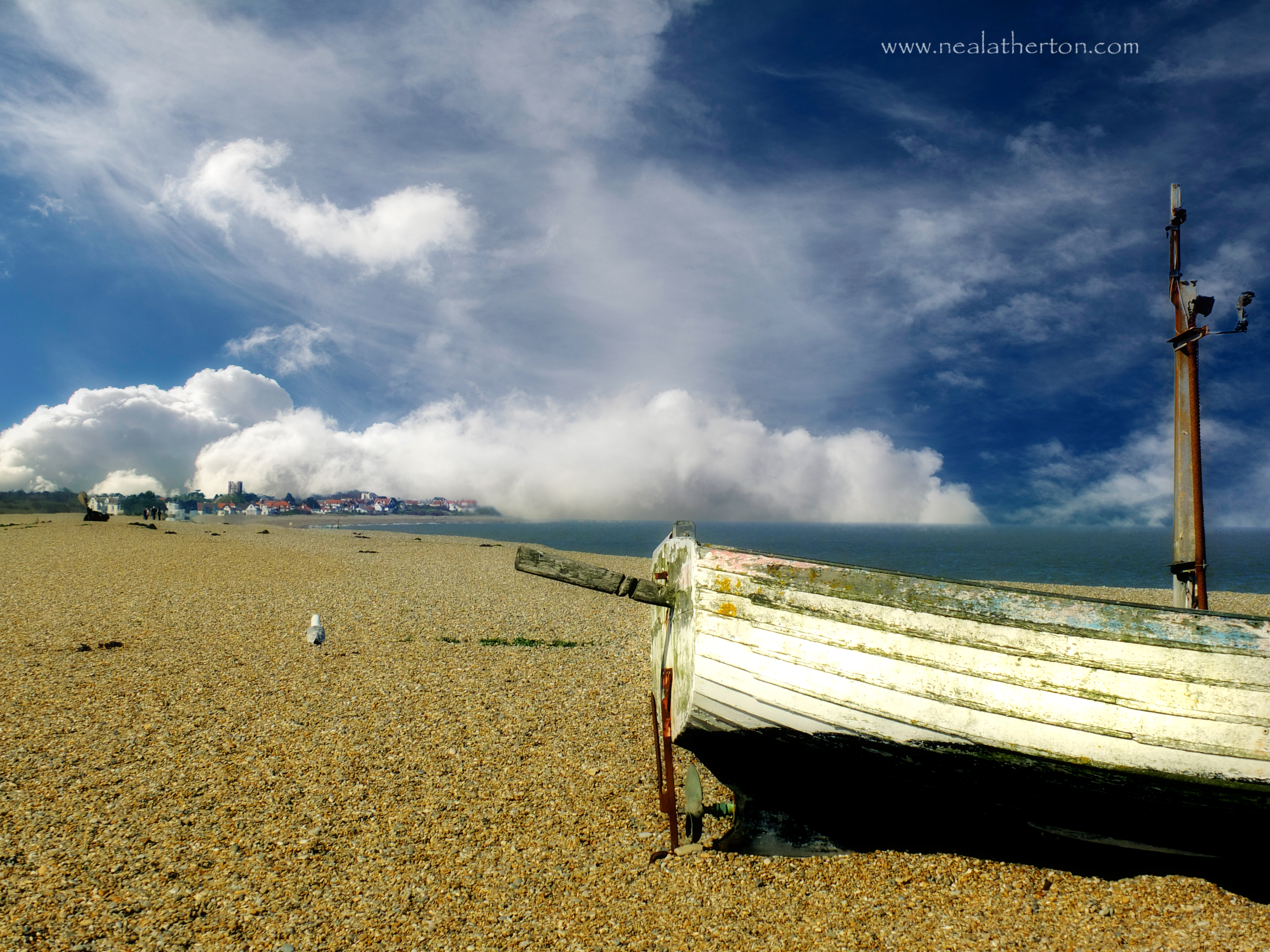 clouds roll over beach and buildings with boat and seagull in foreground suffolk england