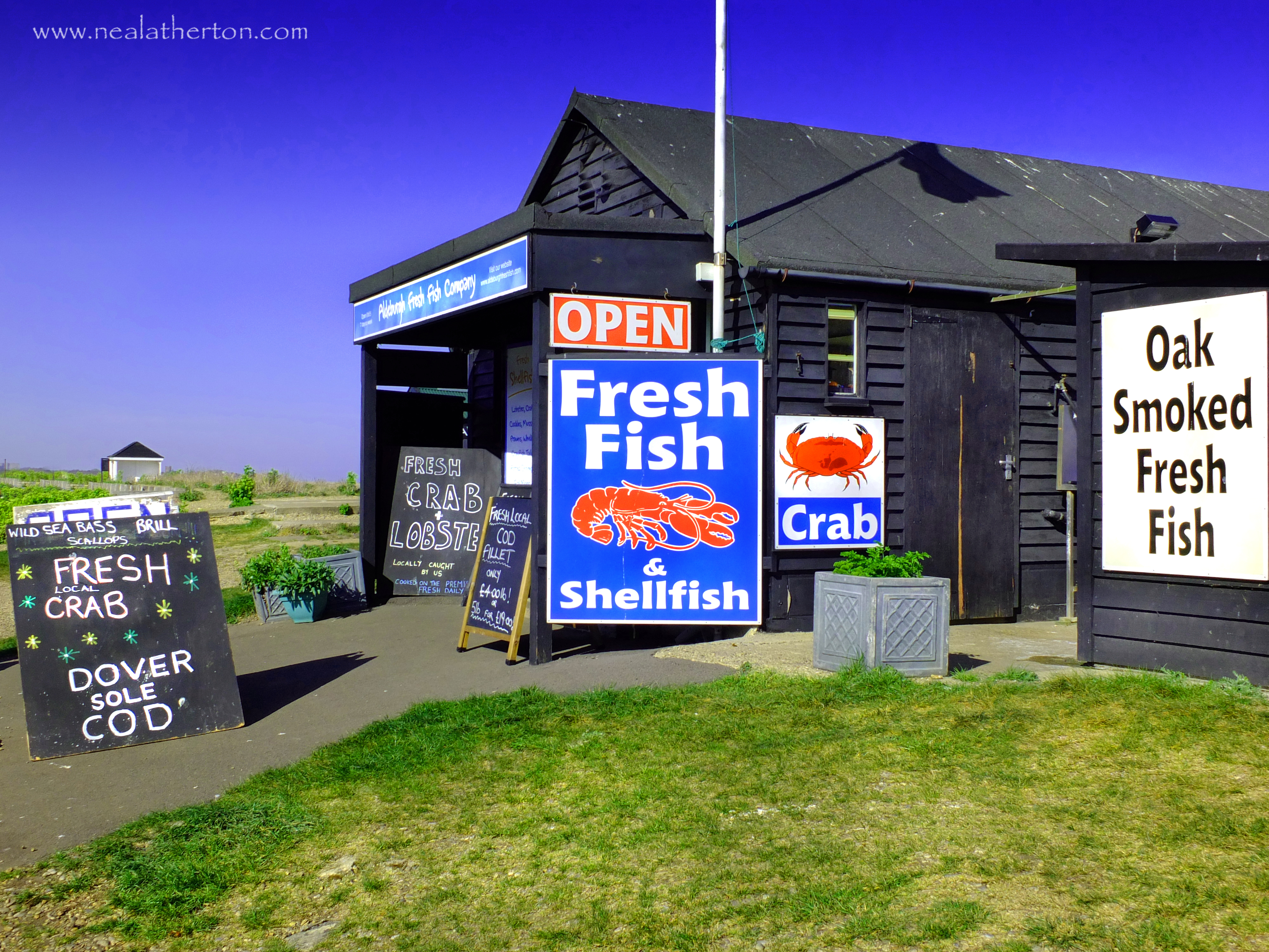 signs displaying fish available from fishing boats in wooden hut with blue summer sky