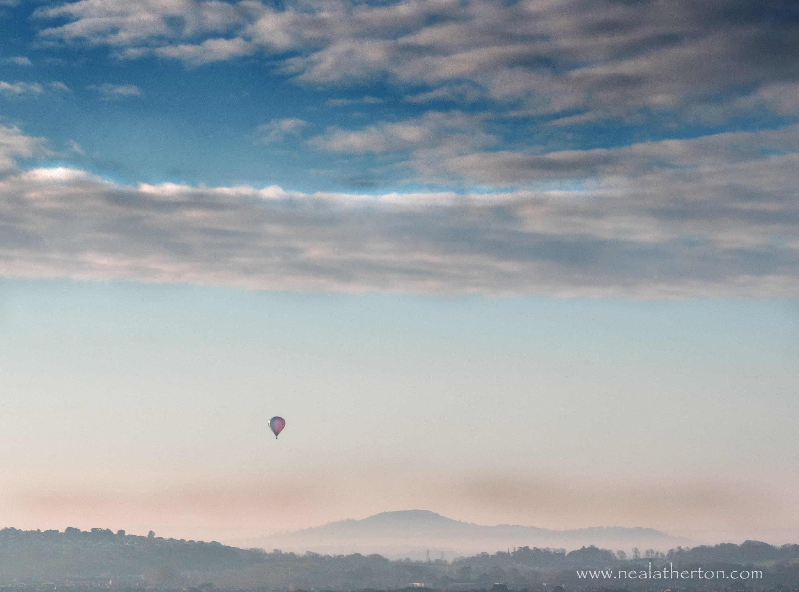 Hot air balloon in early morning blue sky over pier in bay in Somerset