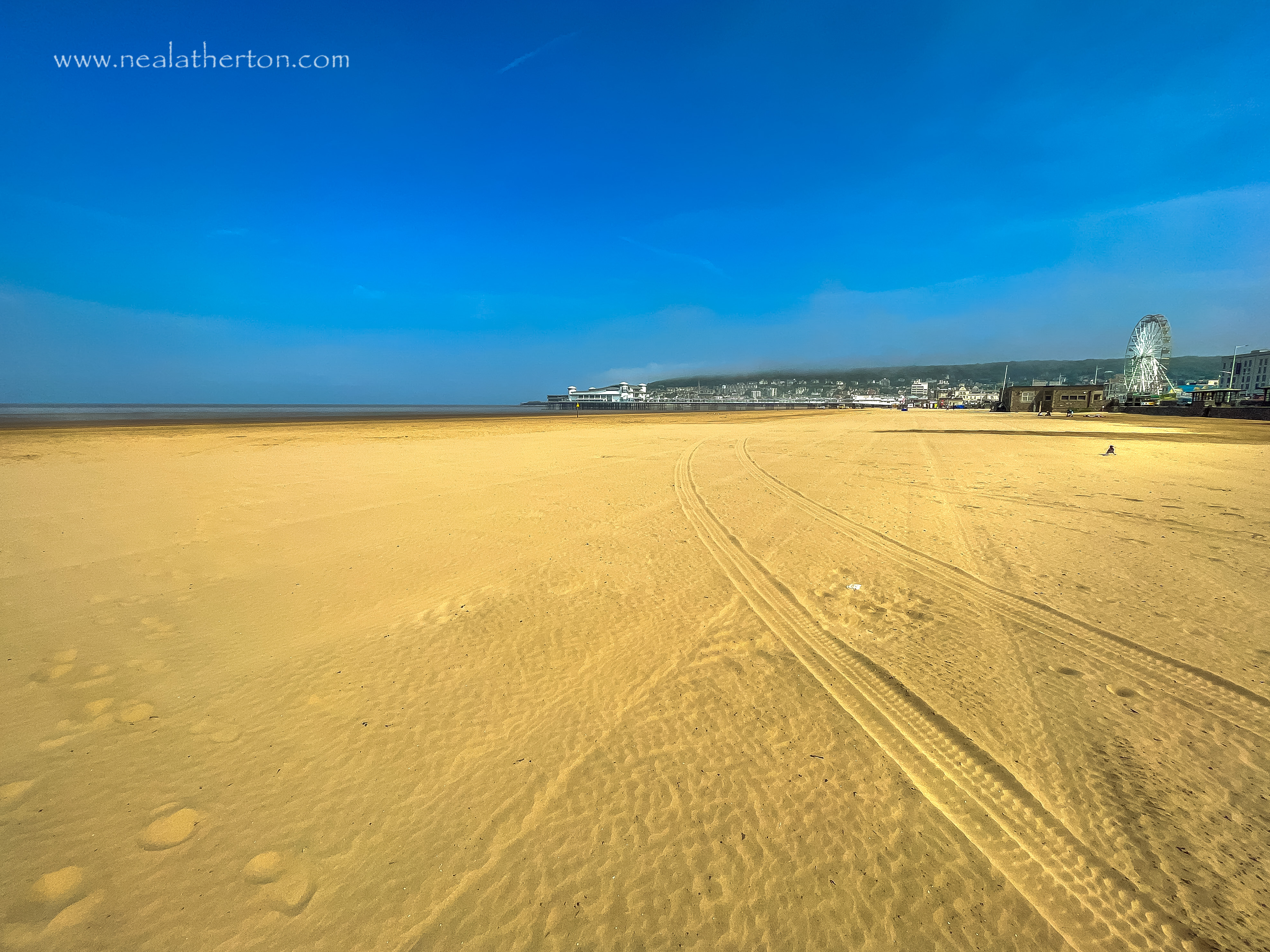 Weston pier and big wheel at the end of sandy beach under hot blue sky in Somerset