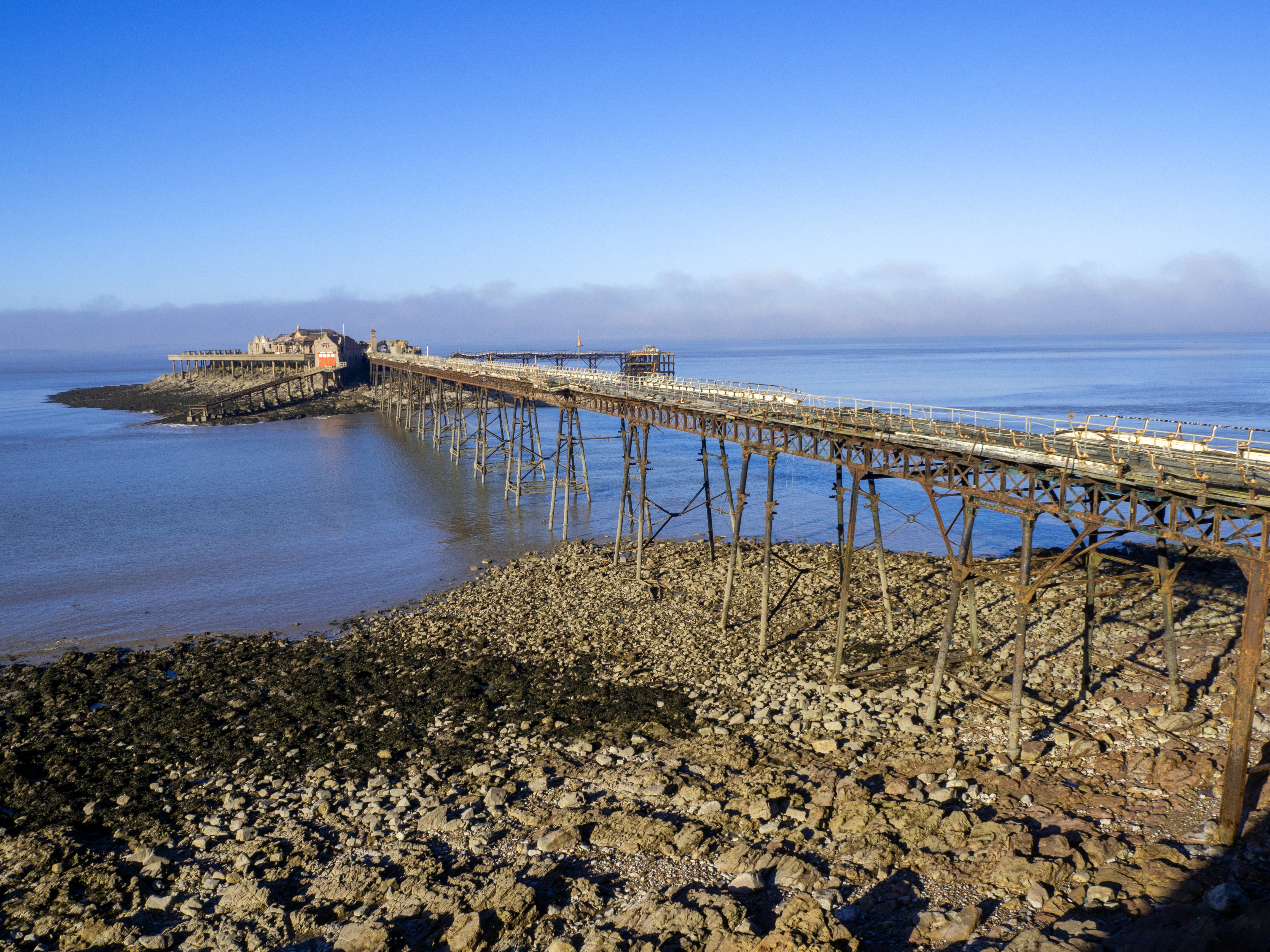 rocky cove in front of old pier with mist over sea and blue sky