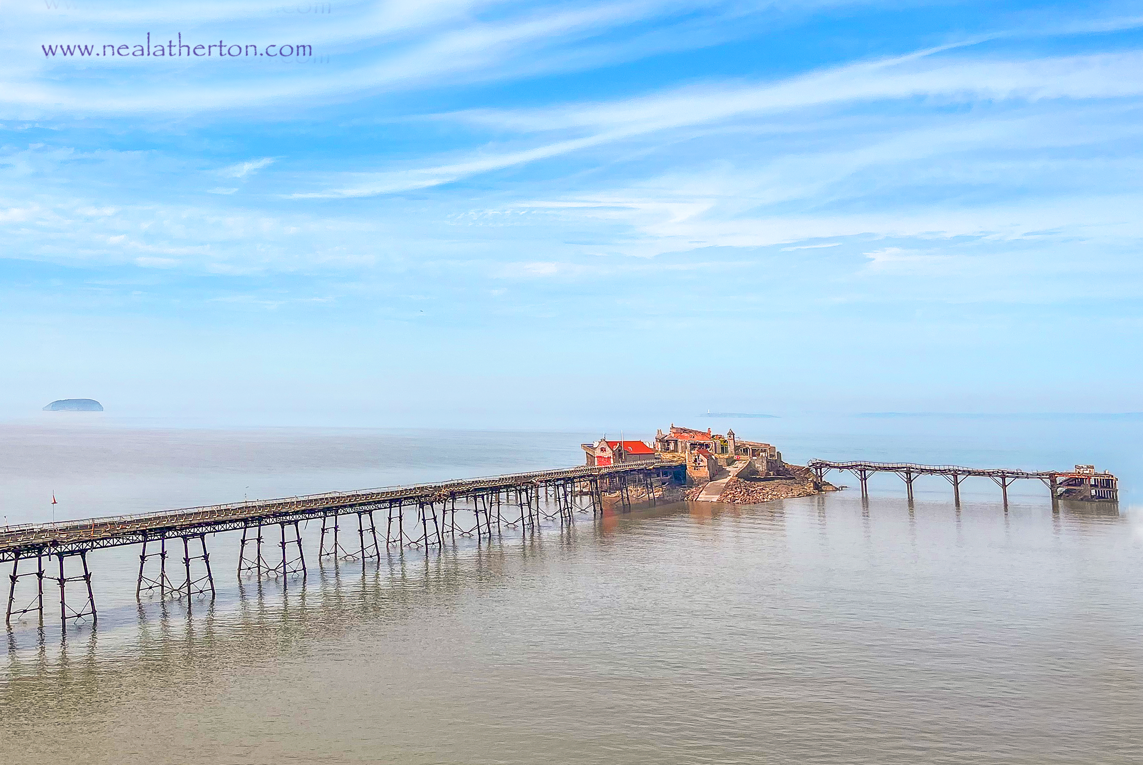 Blue sky and mist with the old pier strtched out in front on a calm sea