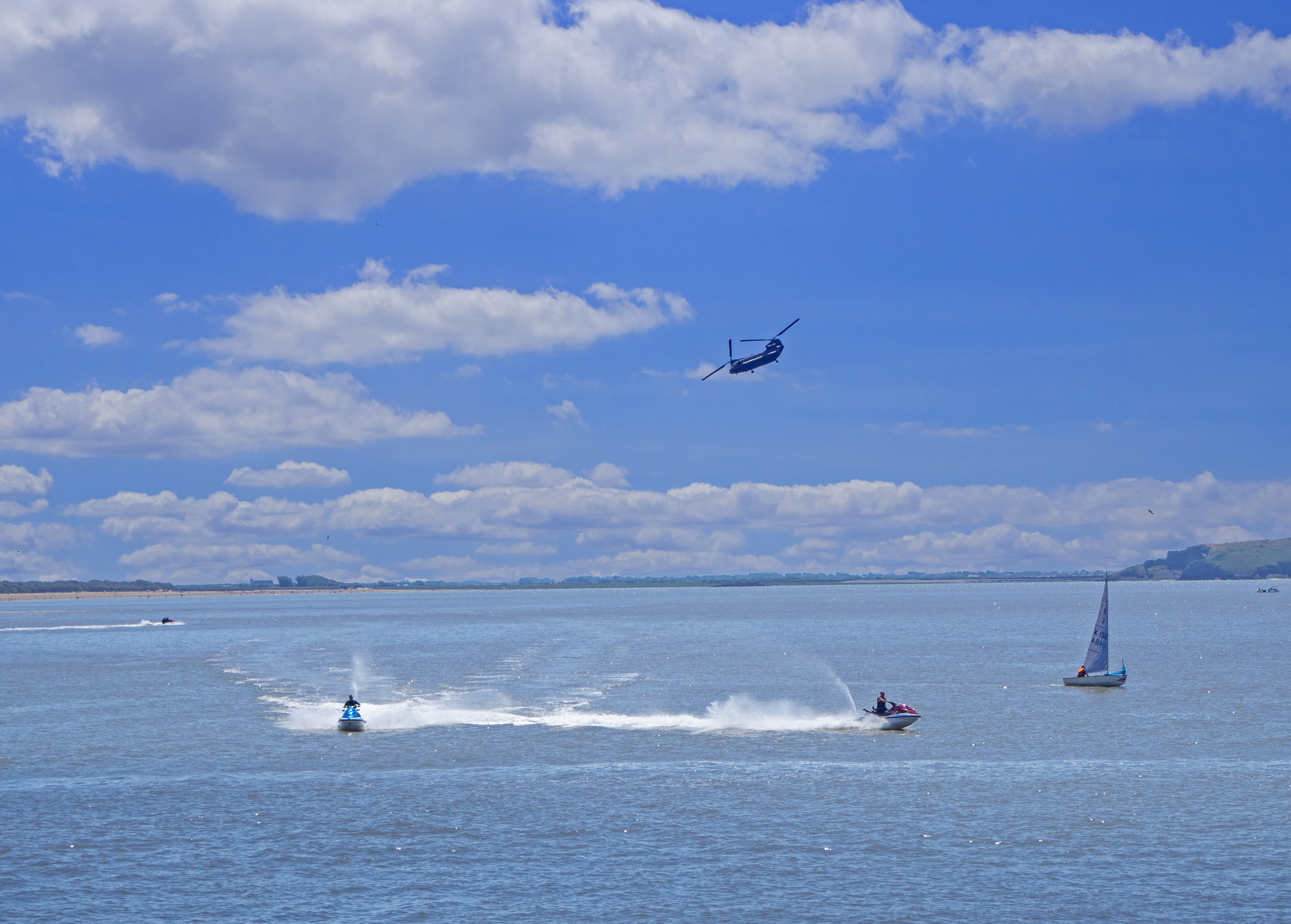 Jetski and yacht with helicopter above in the bay at Somerset on summers day with blue sky and white clouds