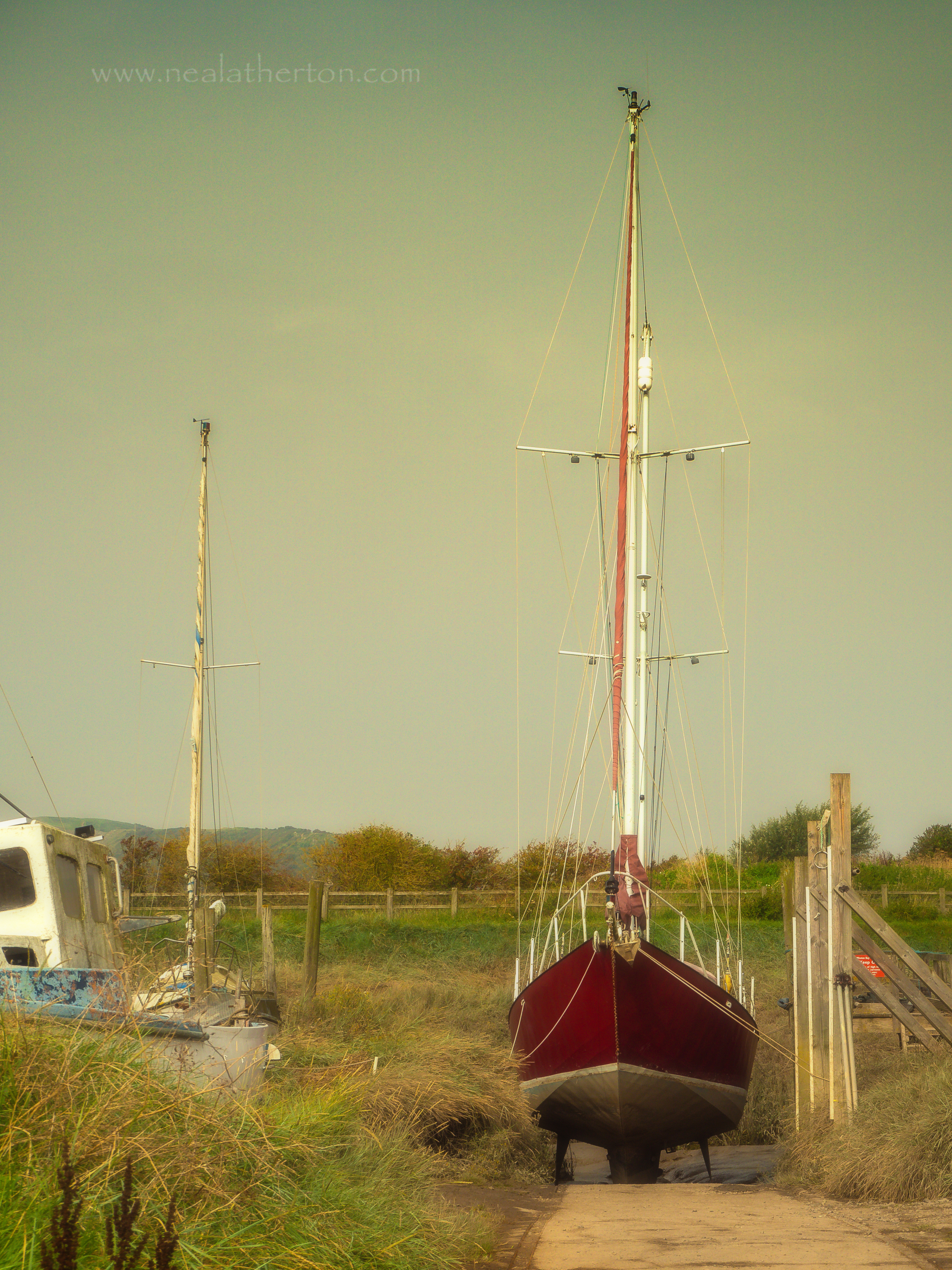 two boats in the boatyard with grass banks in the distance with a moody summer sky