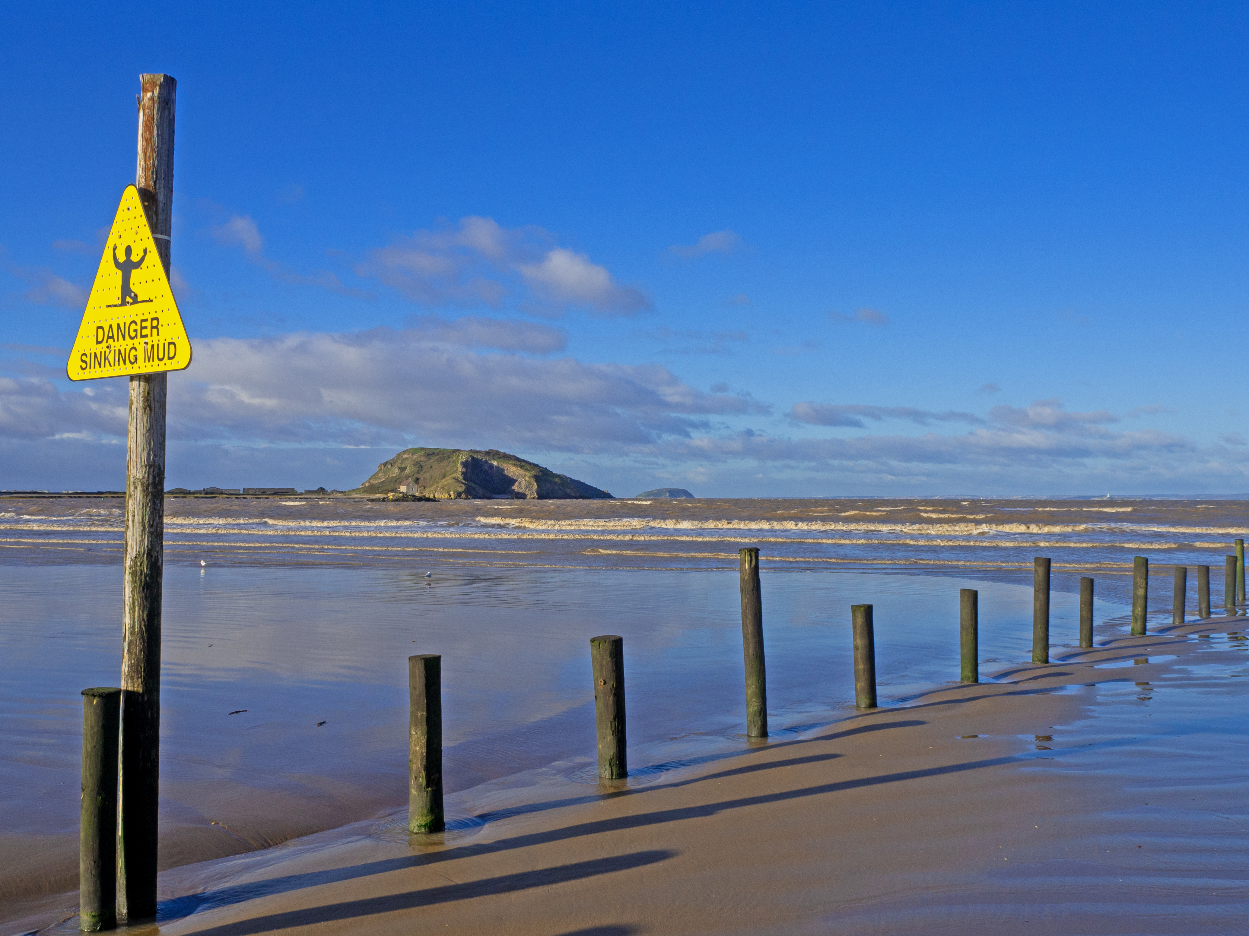 sign and wooden posts on beach with sea and island and blue sky