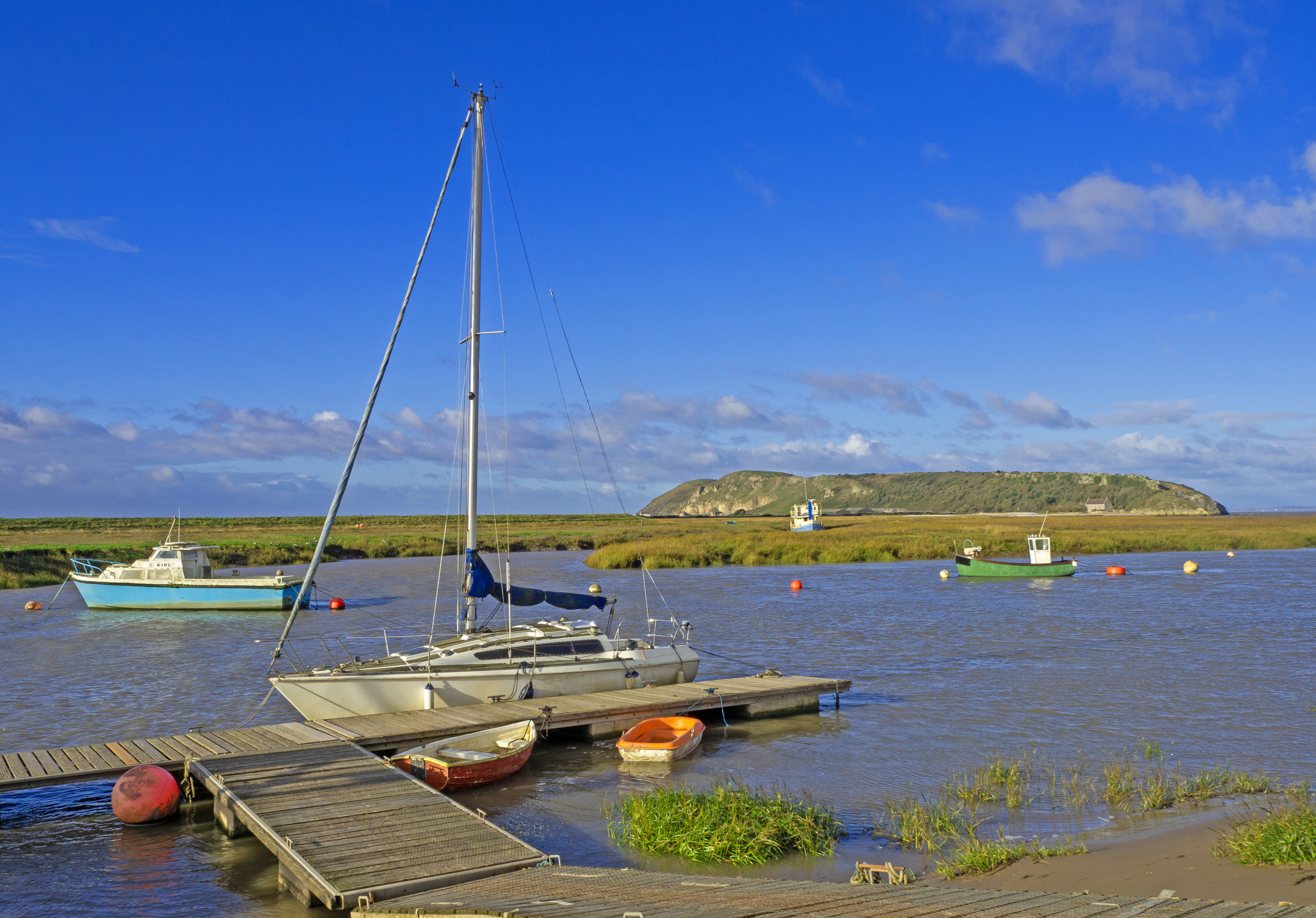 jetty with tacht and boats on river high tide with island and blue sky