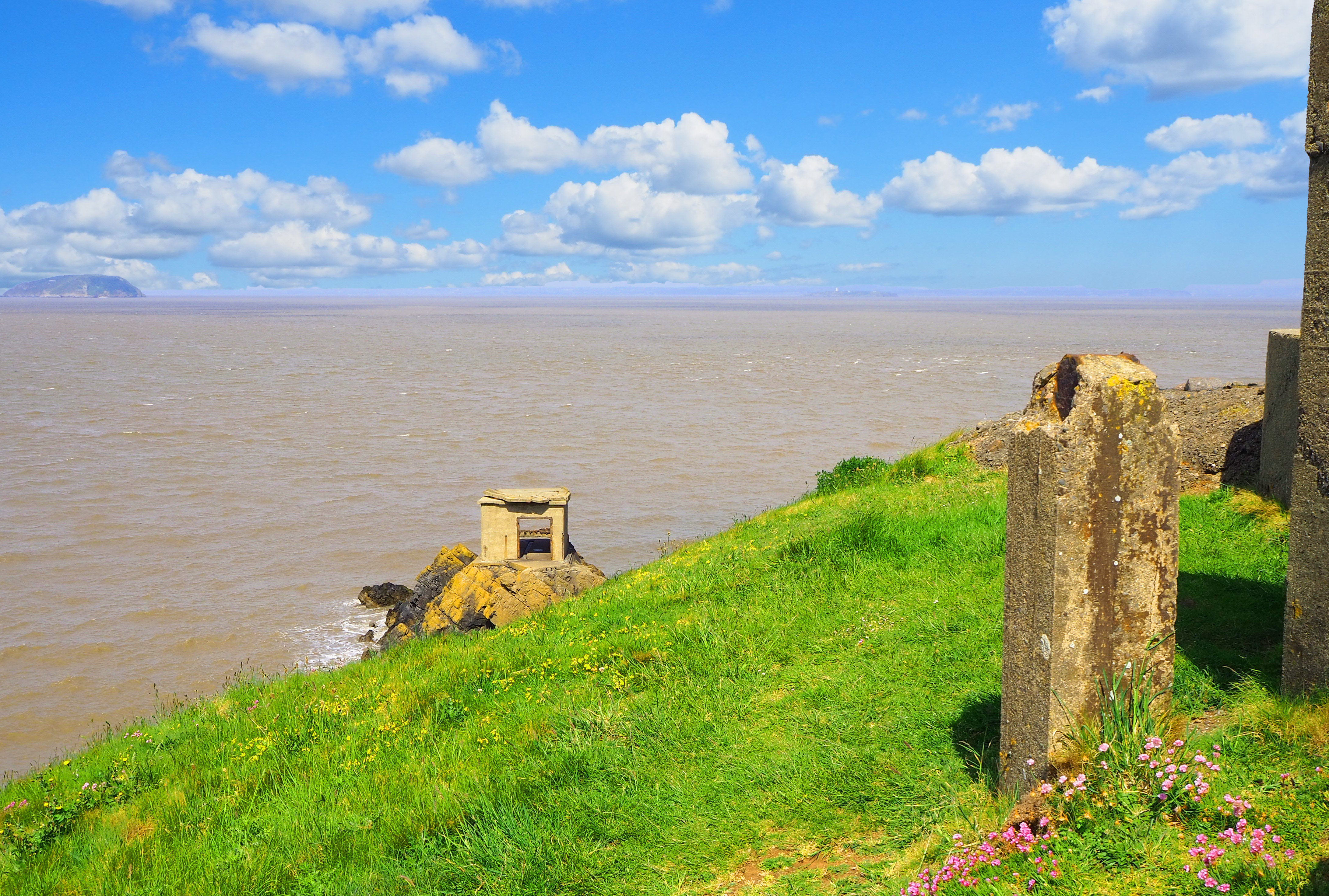 concrete pst and oillbox on grassy headland by sea and island in distance