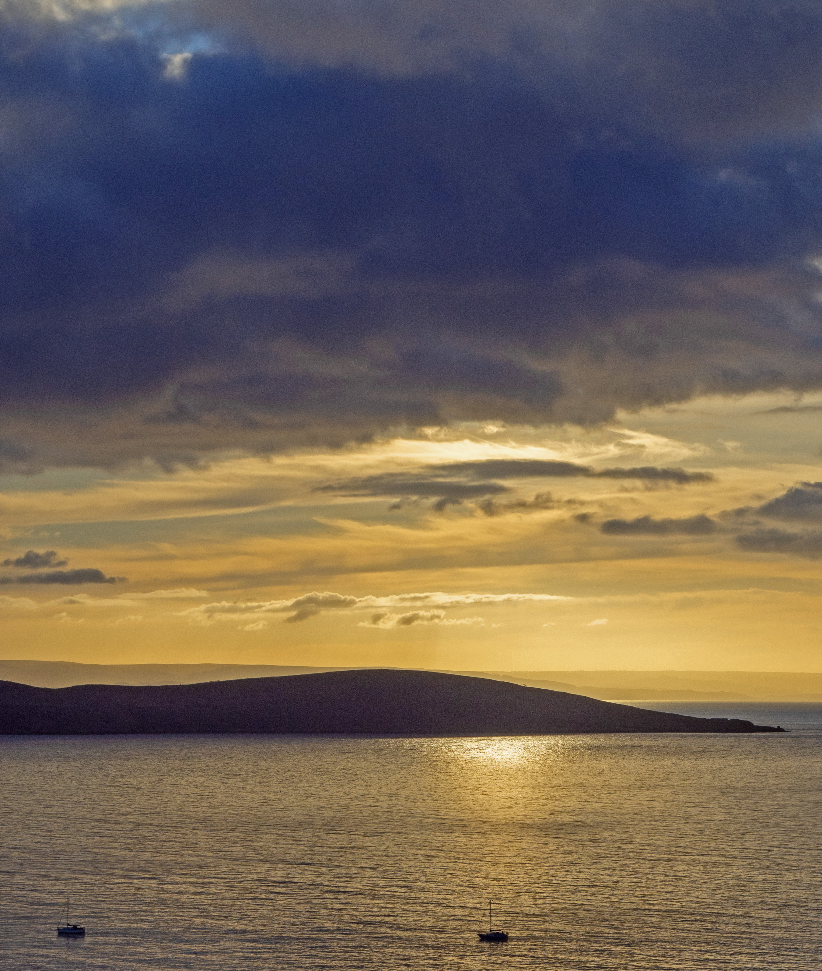 two boats sail on calm sea before island at sunset