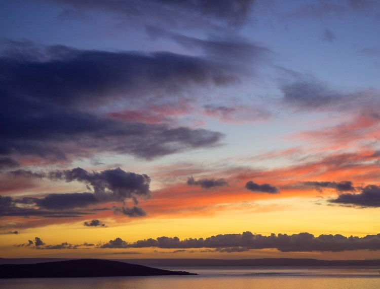 Floating clouds at colourful sunset in somerset with calm sea and island