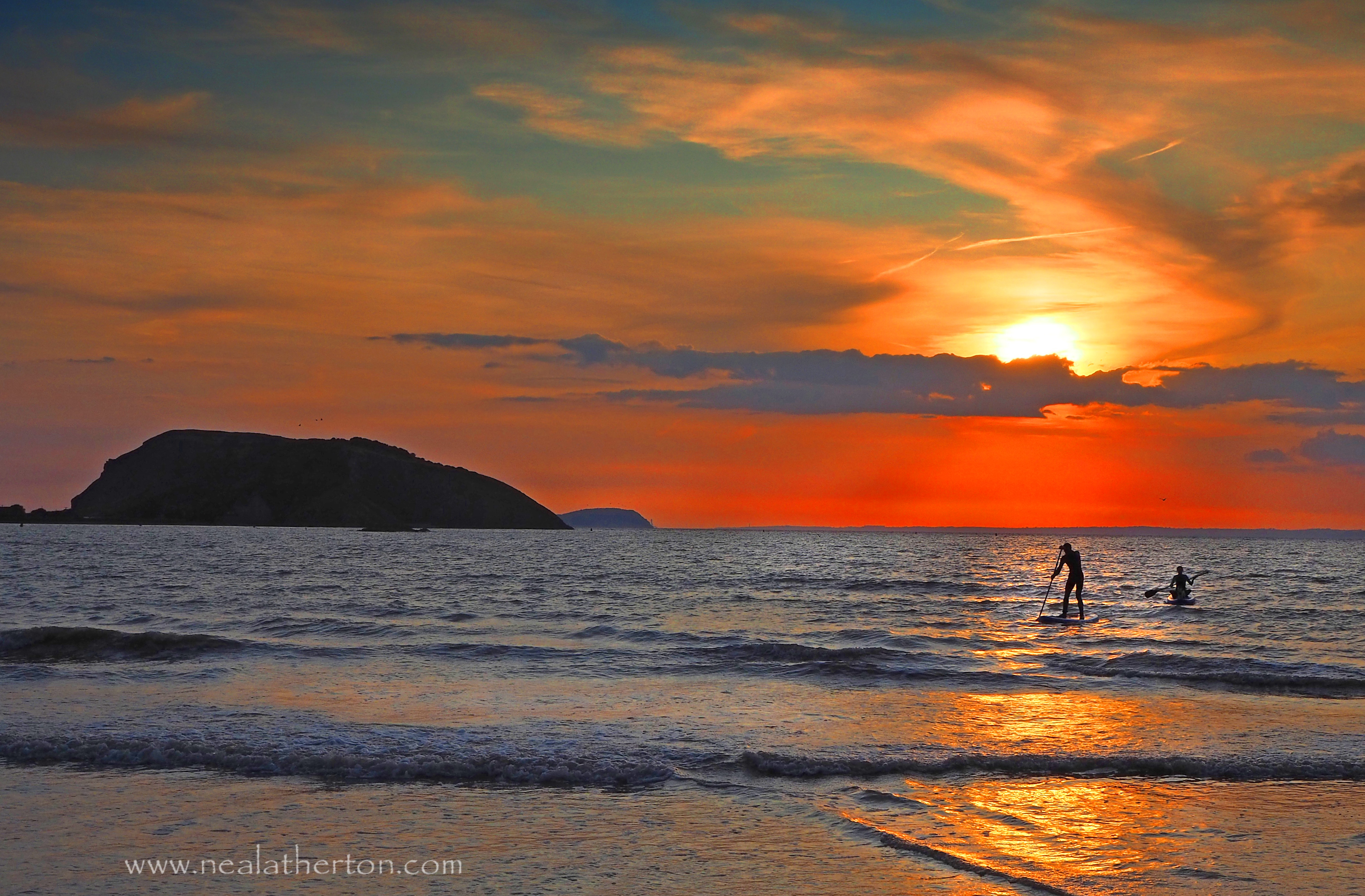 two people paddleboarding in front of island with red sunset and calm sea
