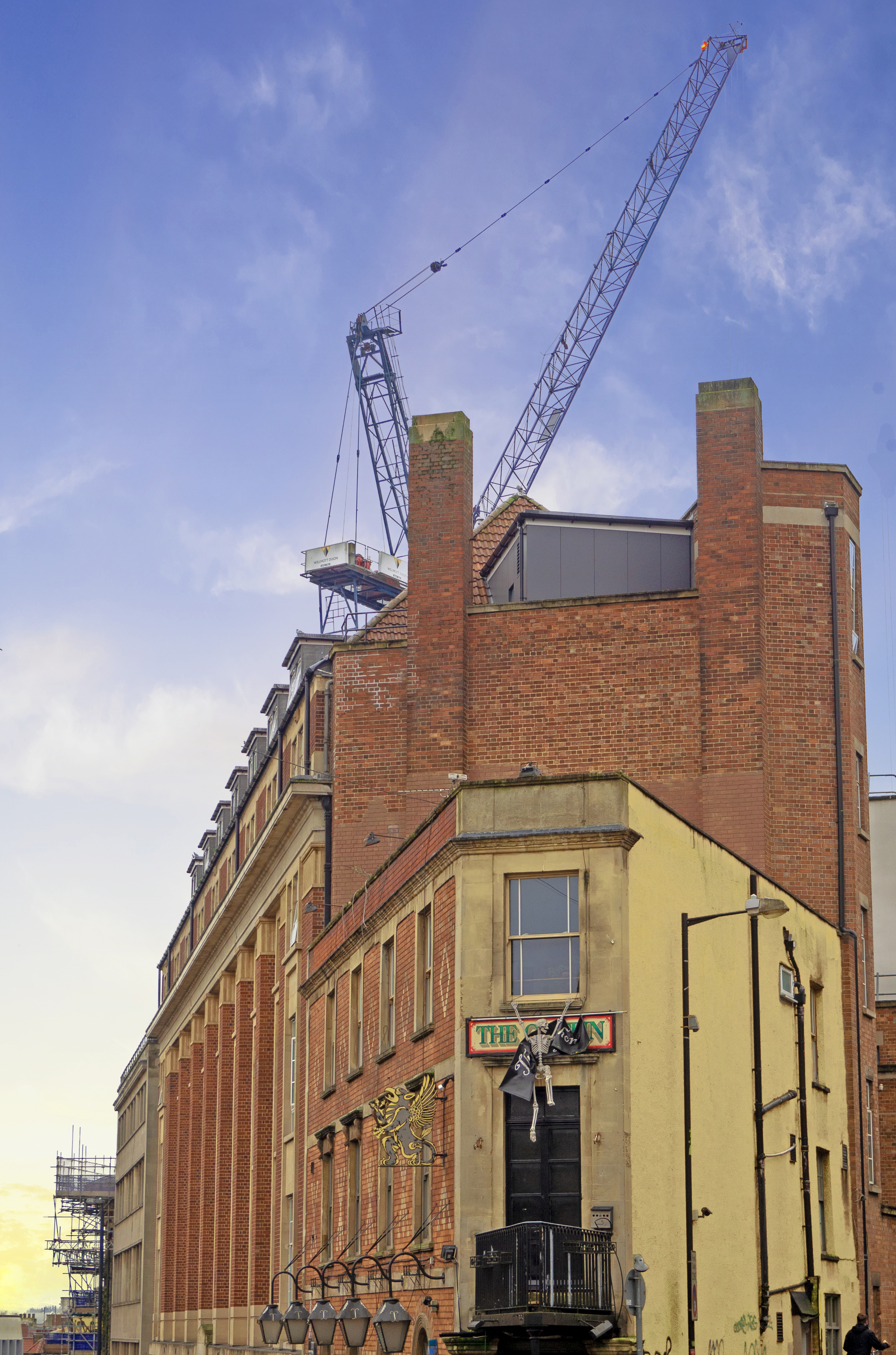 old pub with sign and flags in bristol england with large crane behind and blue sky