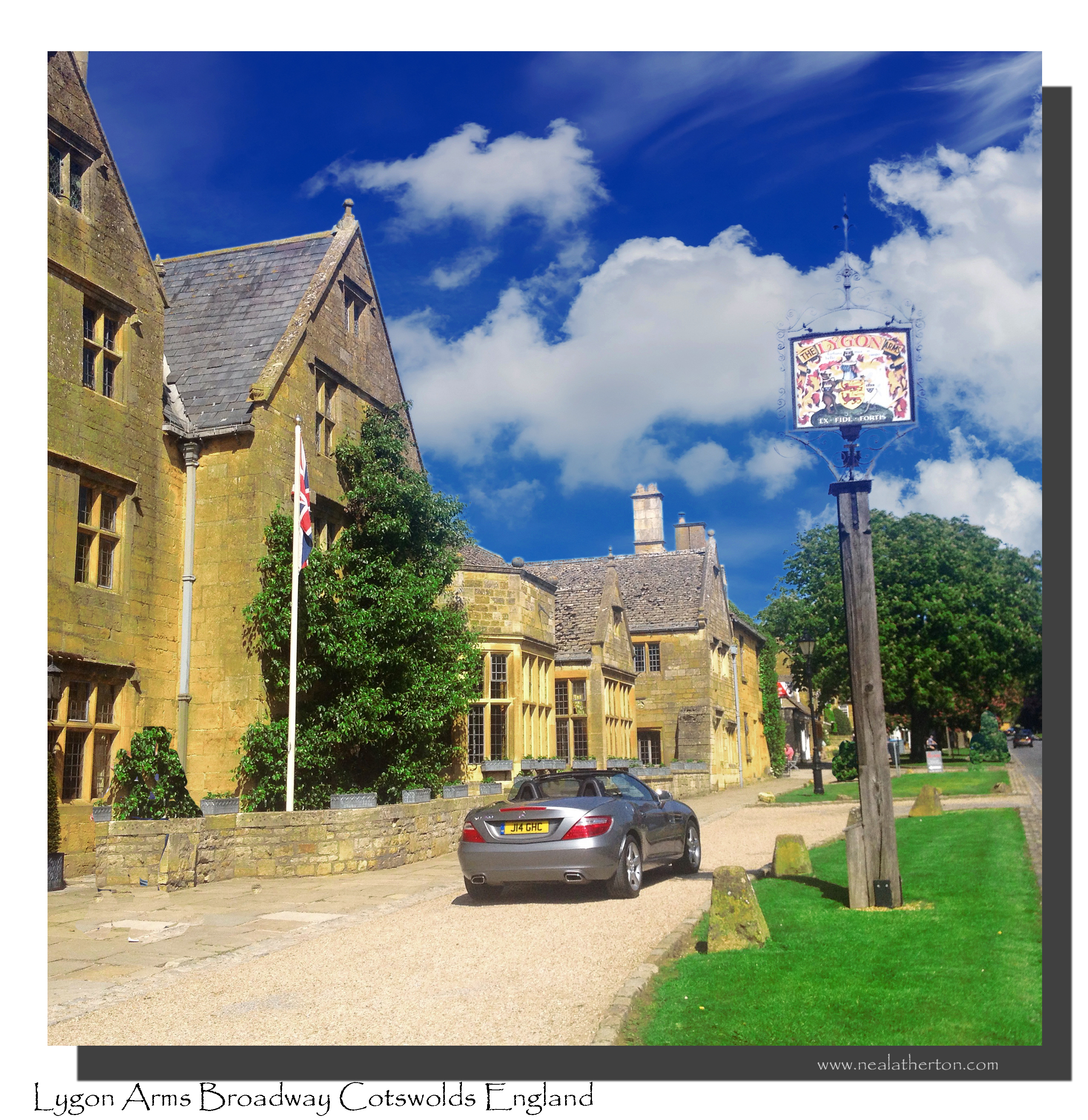 open top car parked by old hotel and trees with flagpole with pub sign and blue sky