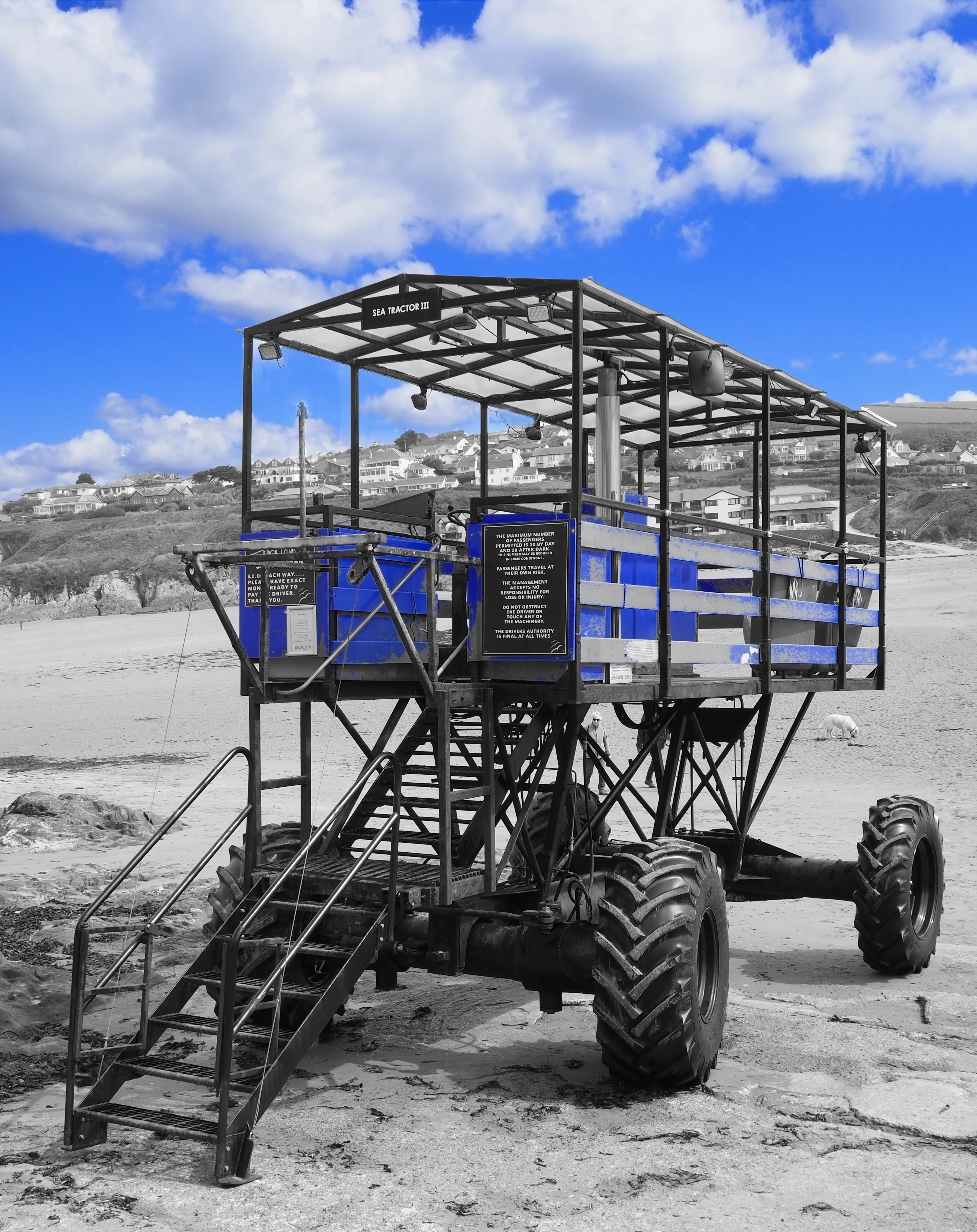 blue sea tractor vehicle on beach with houses on hillside