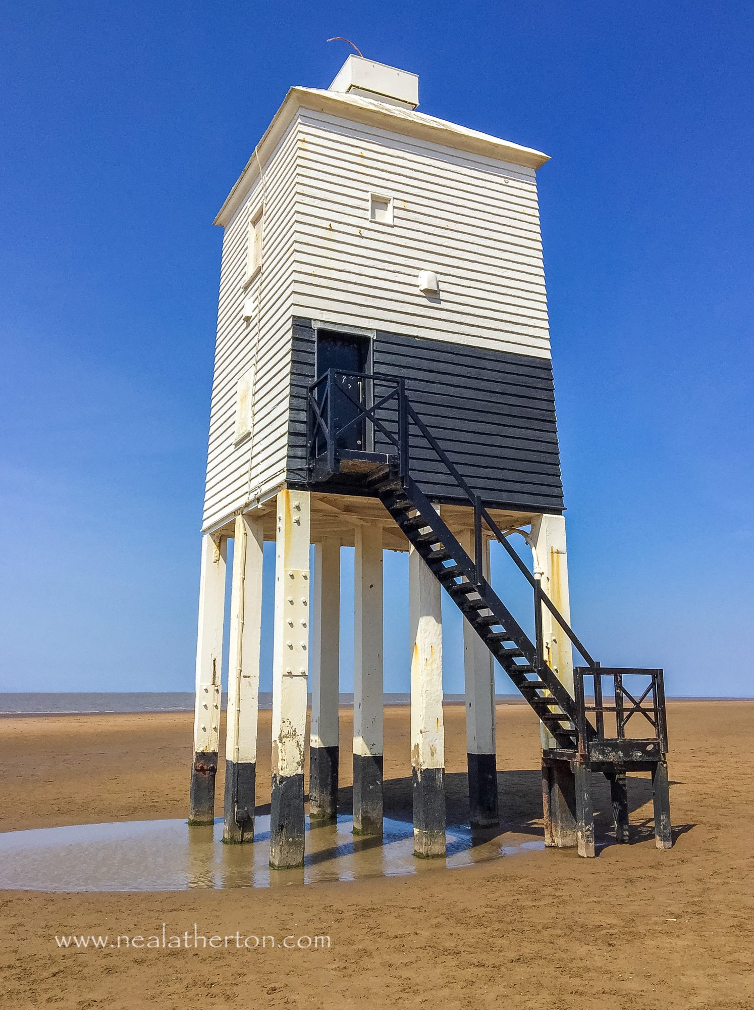 beach with wooden lighthouse with steps and sea with blue sky