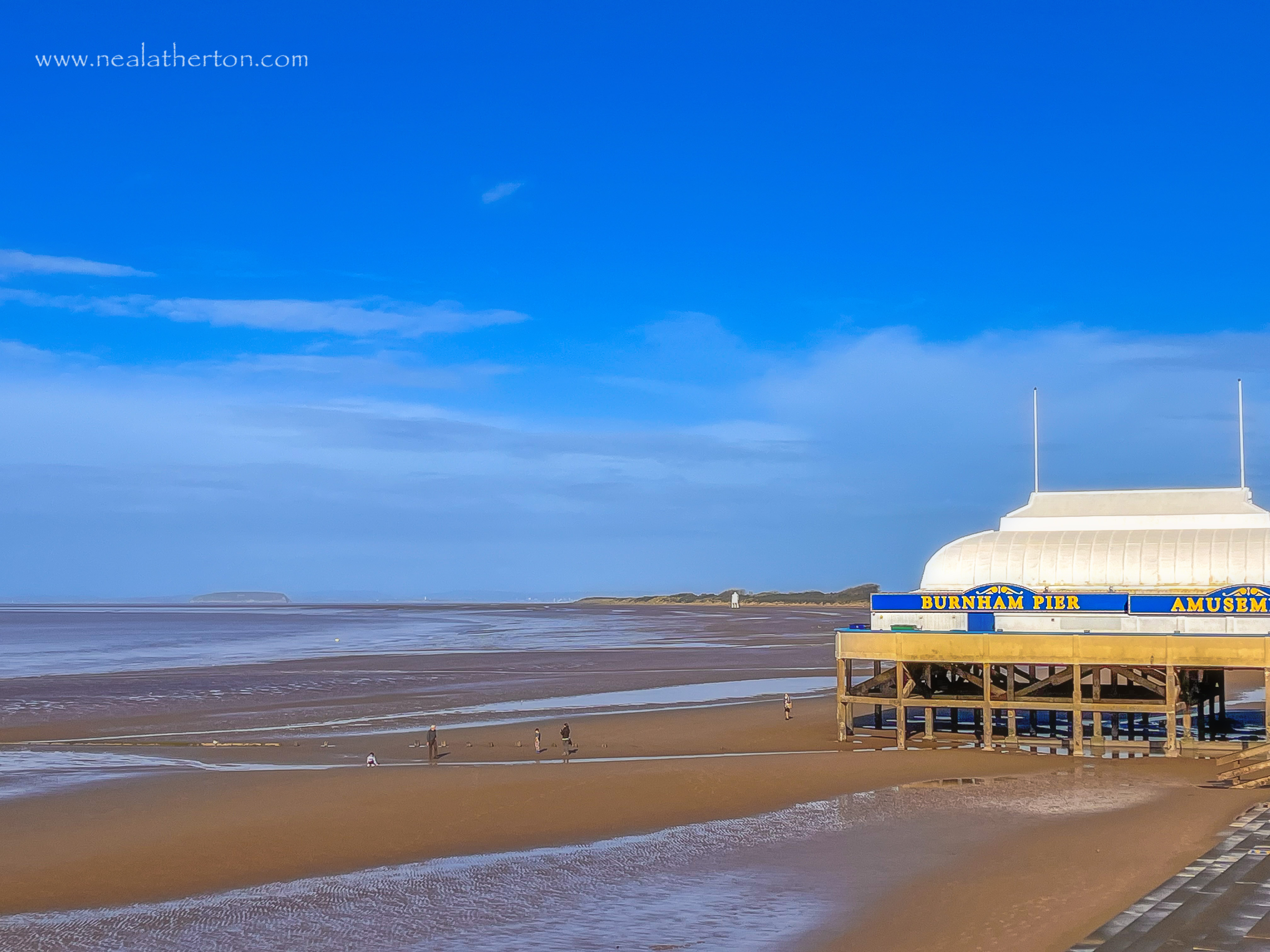 beach with old white pier with people and dogs near sea and blue sky