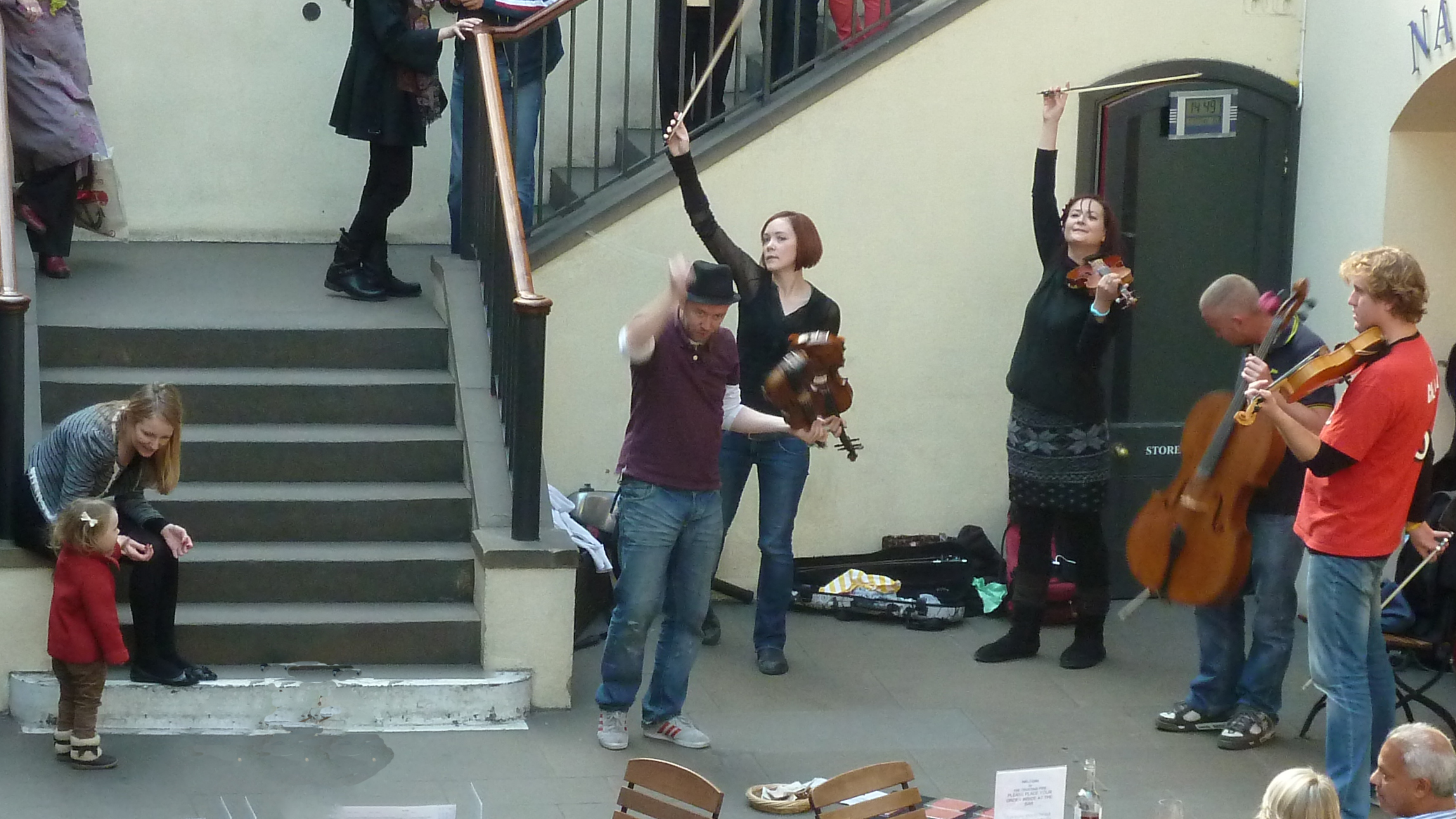 Musicians with violins and chello in market with stone steps and mother and child