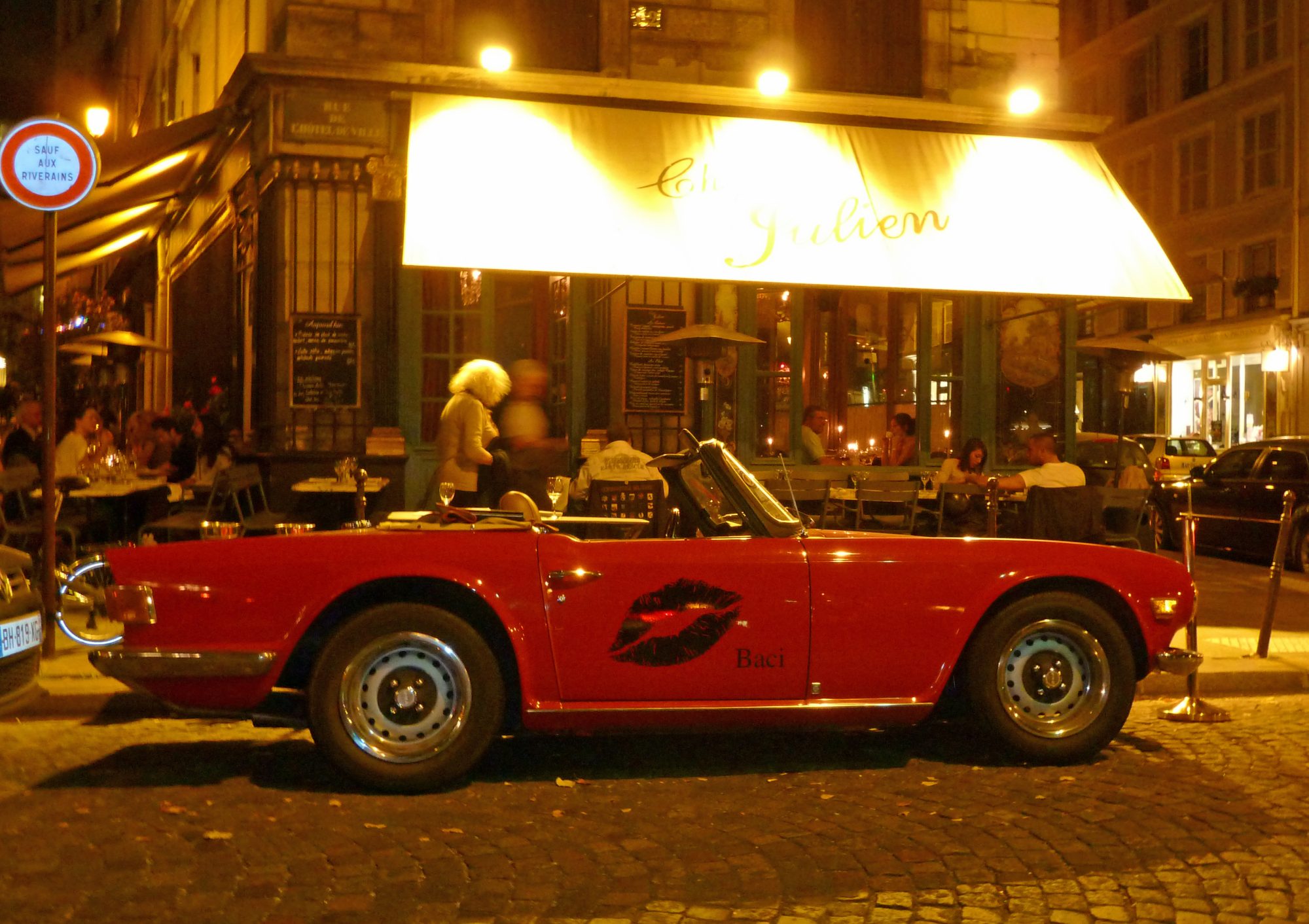 Red sports car on cobbled steet with restaurant and people eating at night