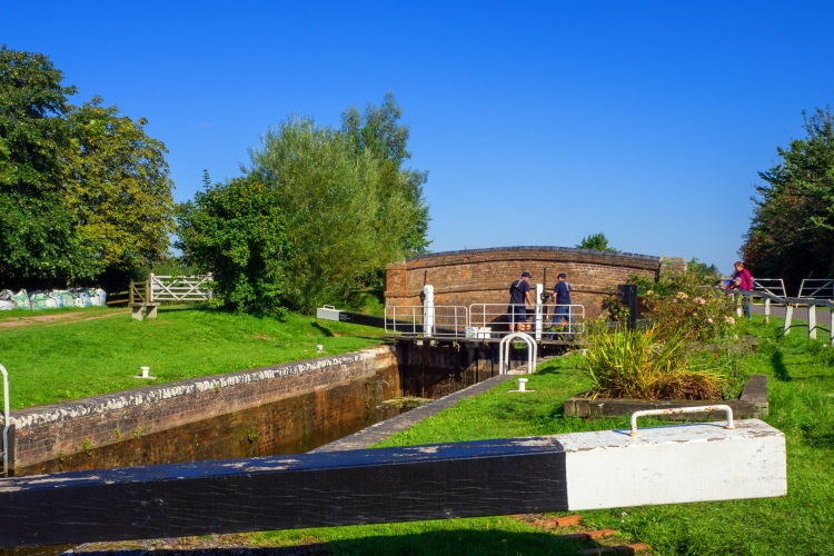 lock gates in front of tunnel bridge on canal with grass and trees and people working