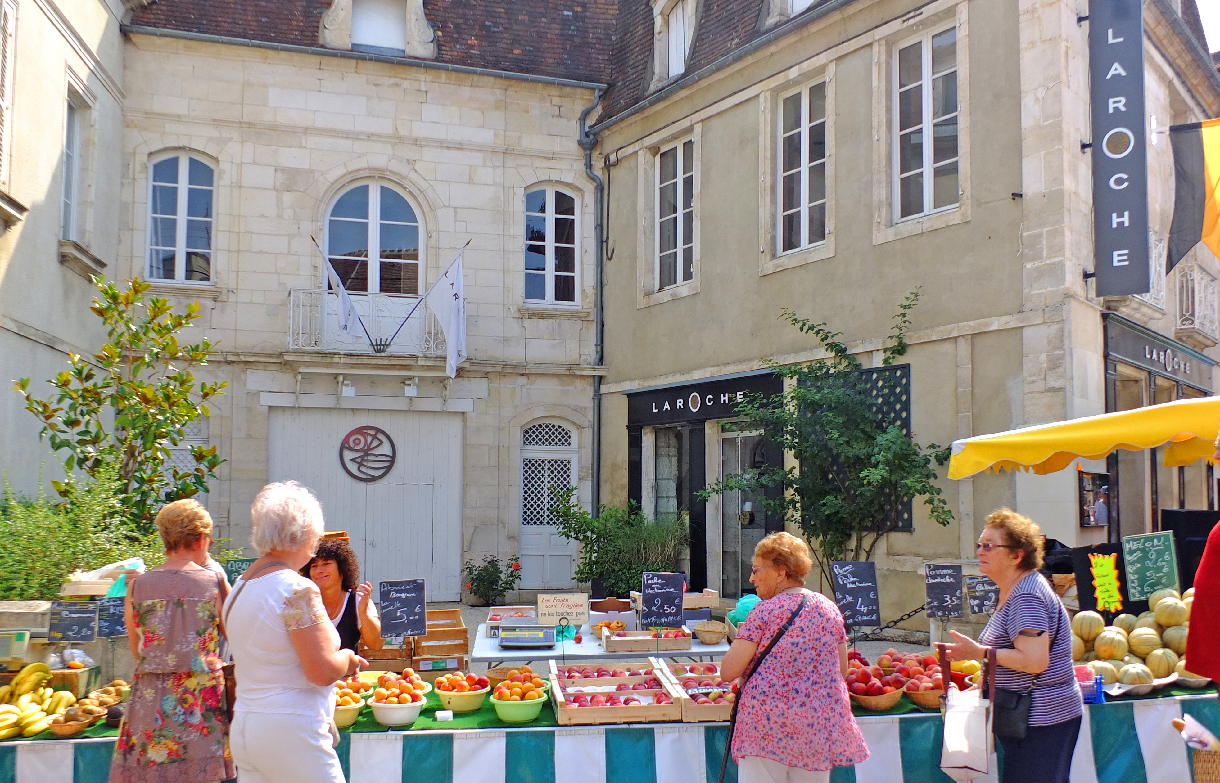 fruit on stall in market with people and old buildings and flags