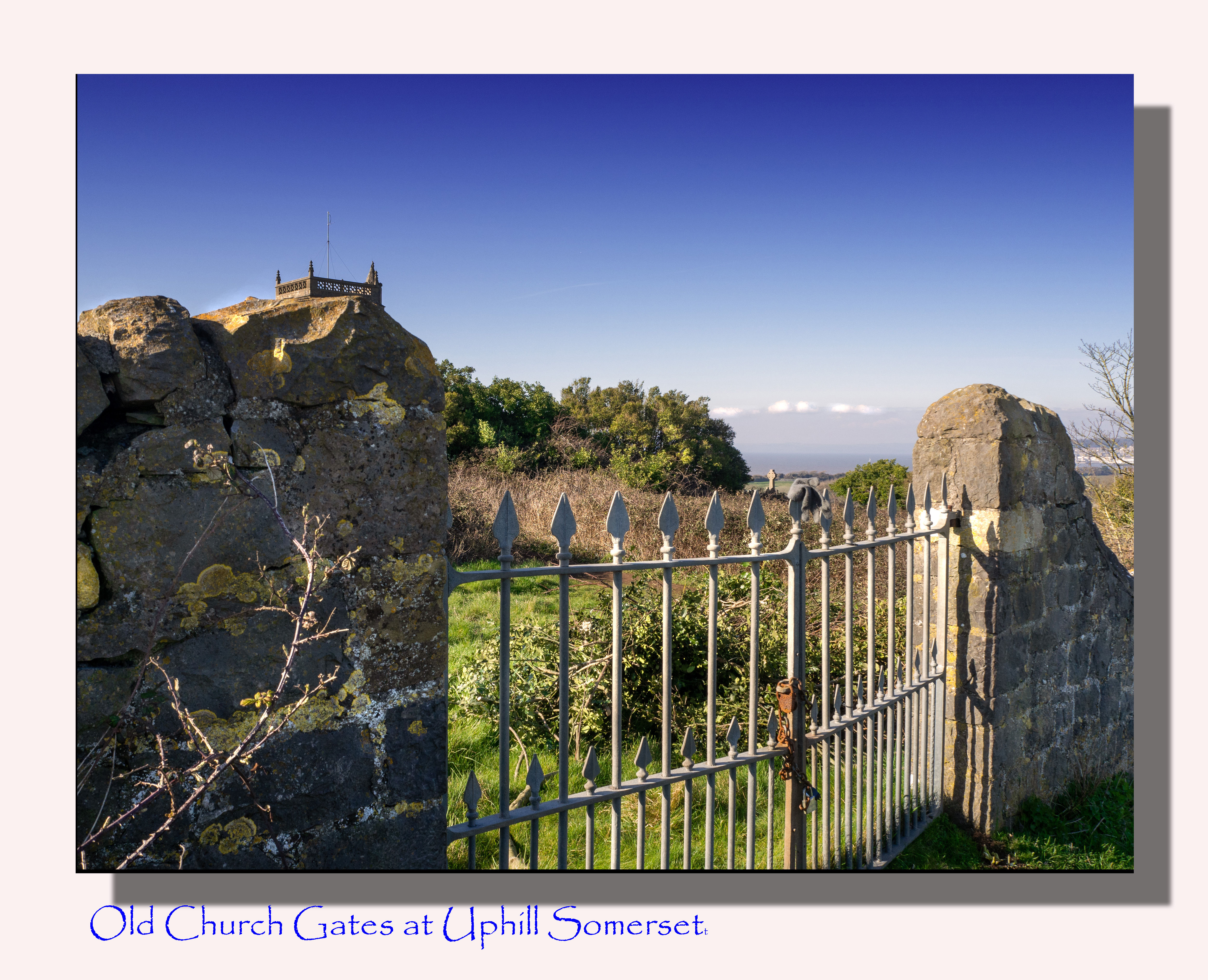 old wall with iron gate with grassy wilderness and blue sky over church
