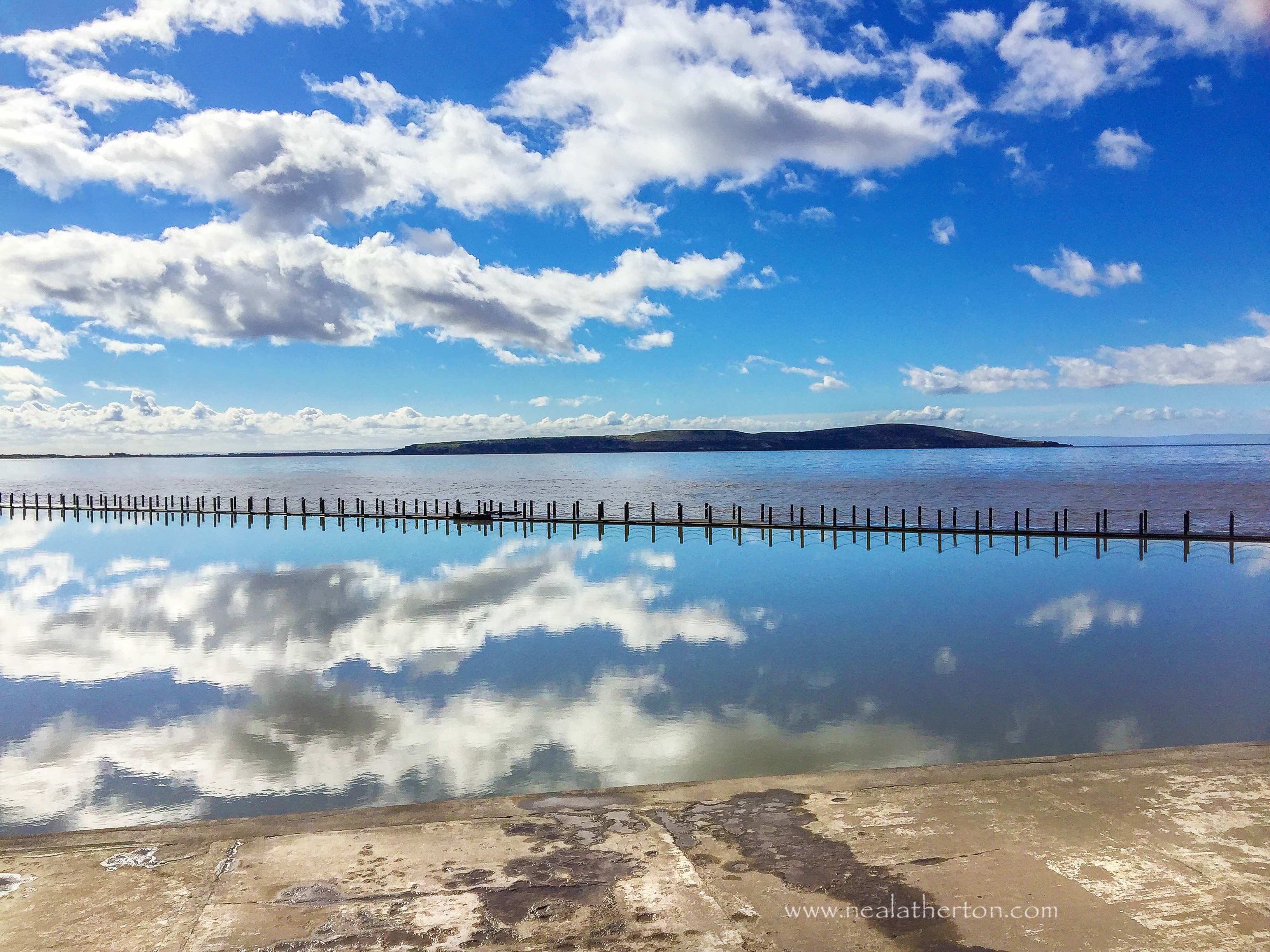 water in lake shows clouds relected in the water as you see Brean Down in the distance of Weston Bay