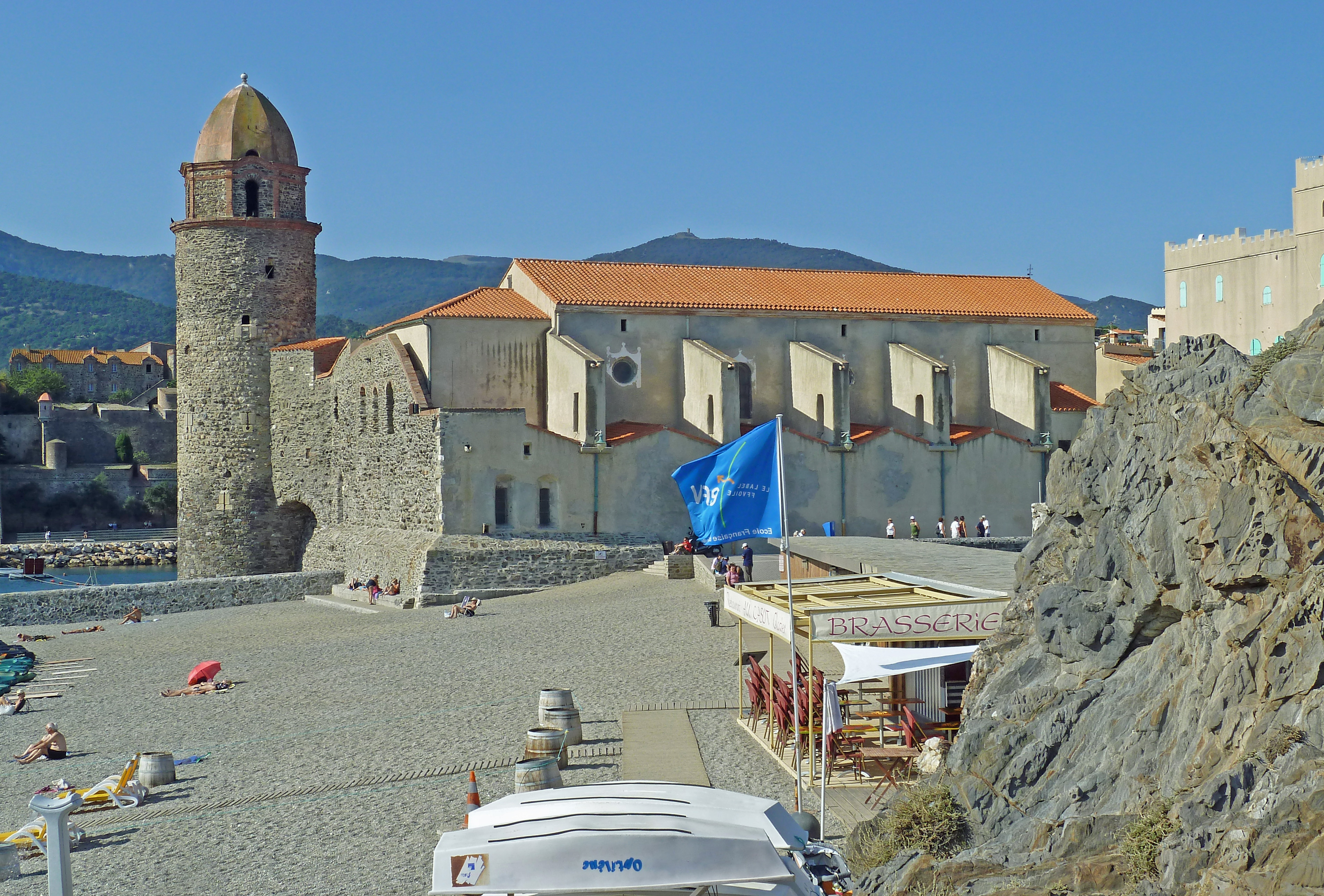 boats on beach with restaurant terrace in front of church and hills