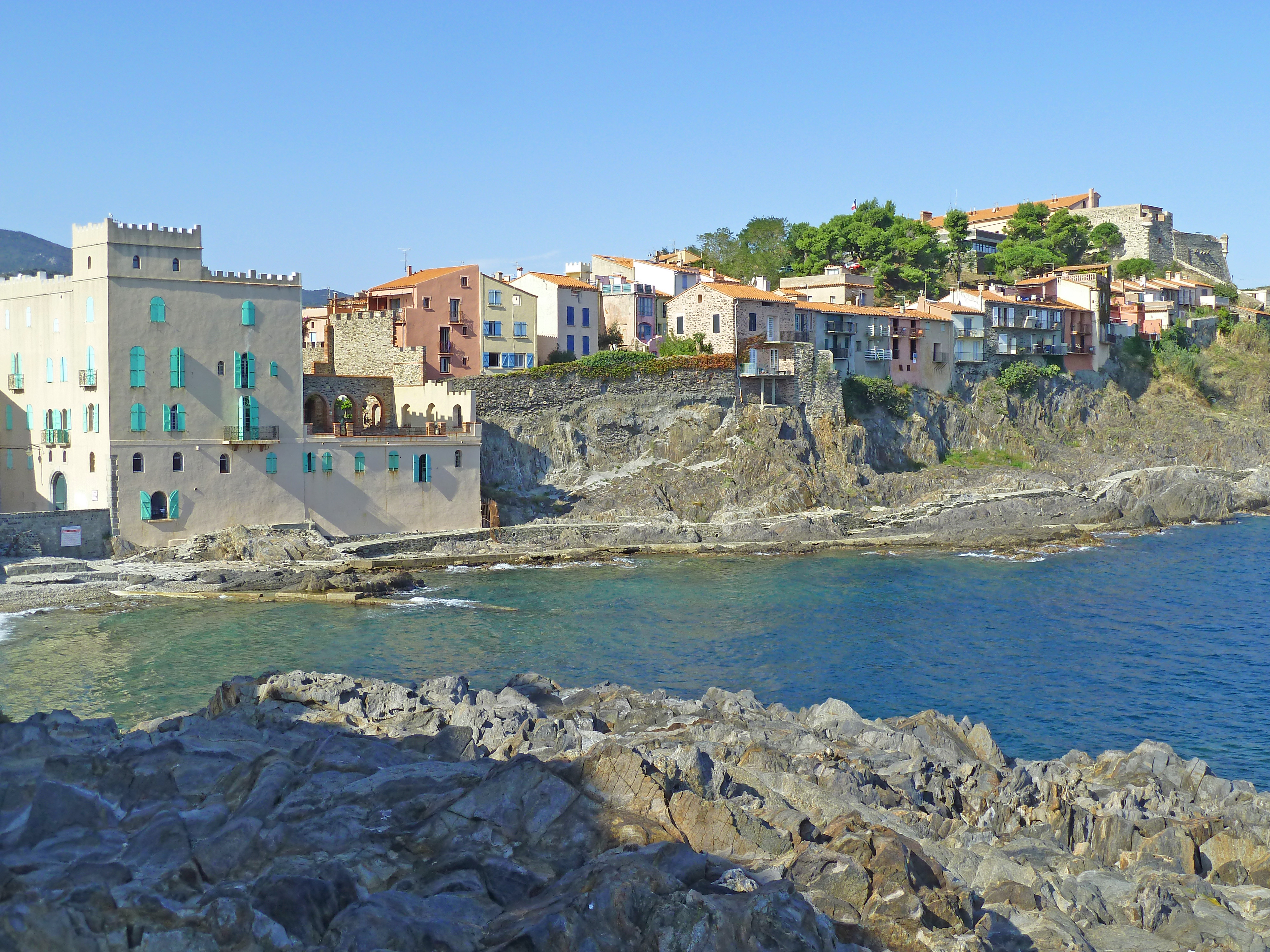 sea lapping into small; beach with rocks and houses rising in hill in summer sky