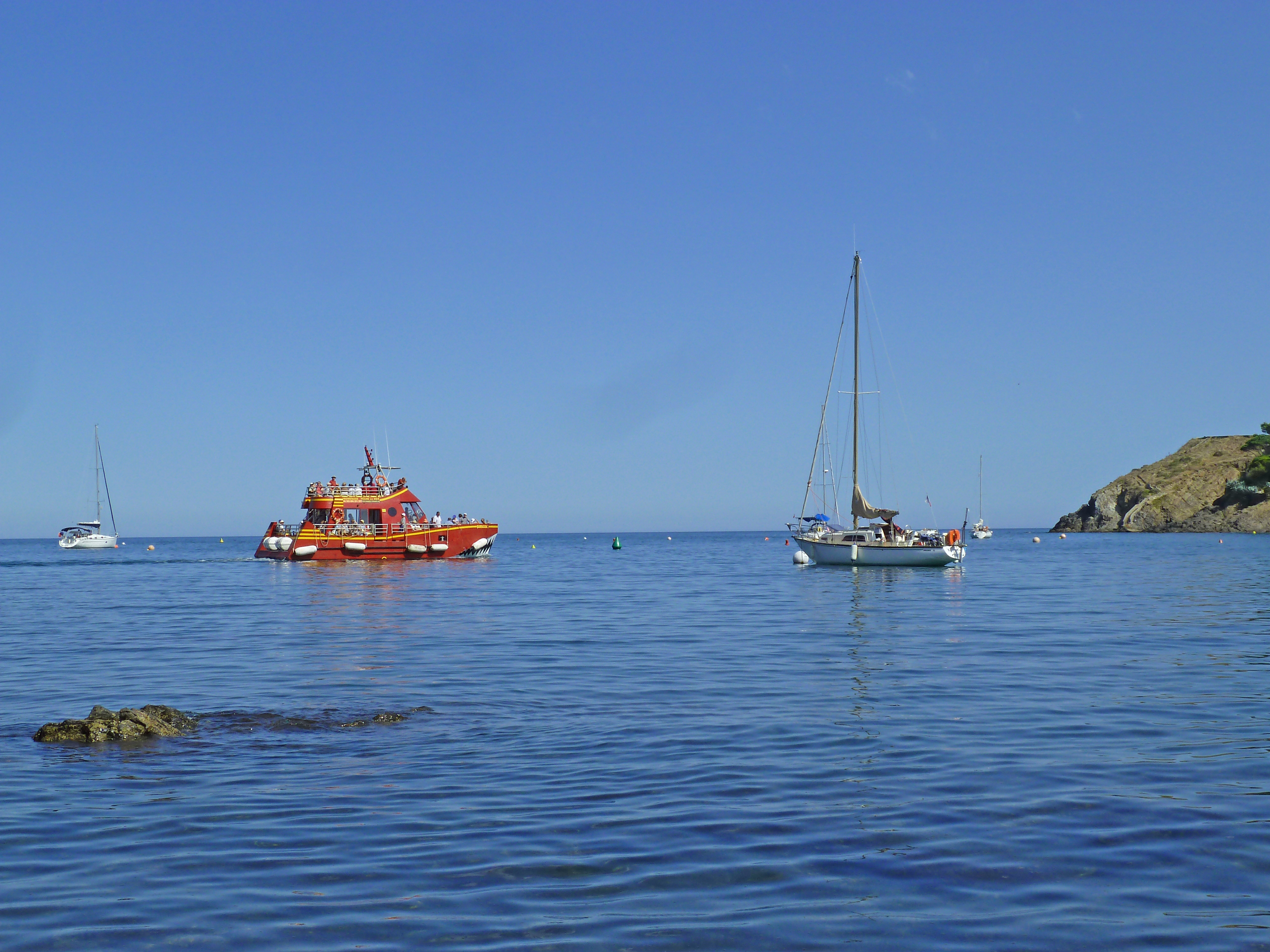 three boats on calm blue sea with rocks and blue sky