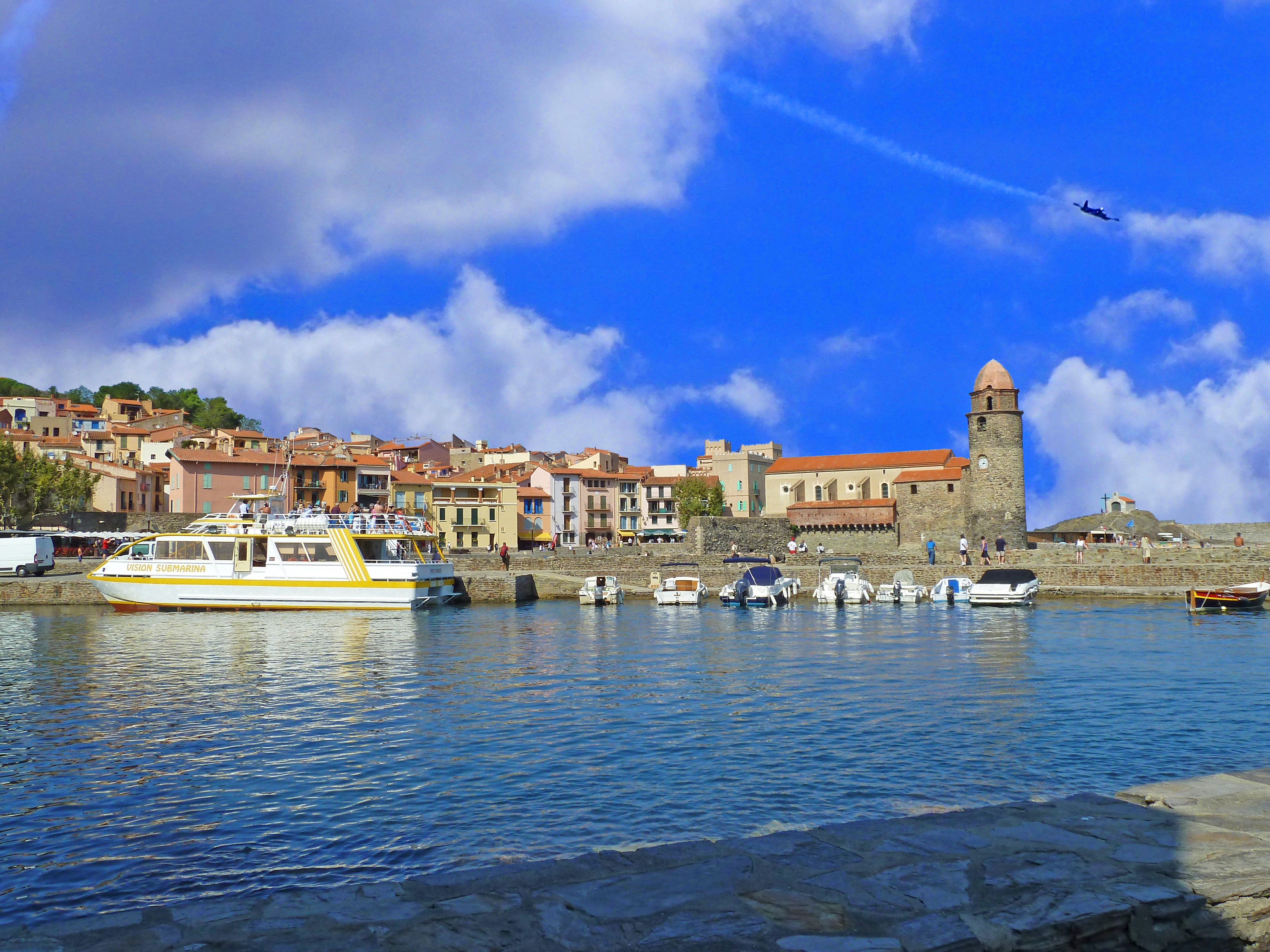 ship and boats in harbour with church and tower and houses around with plane in blue sky