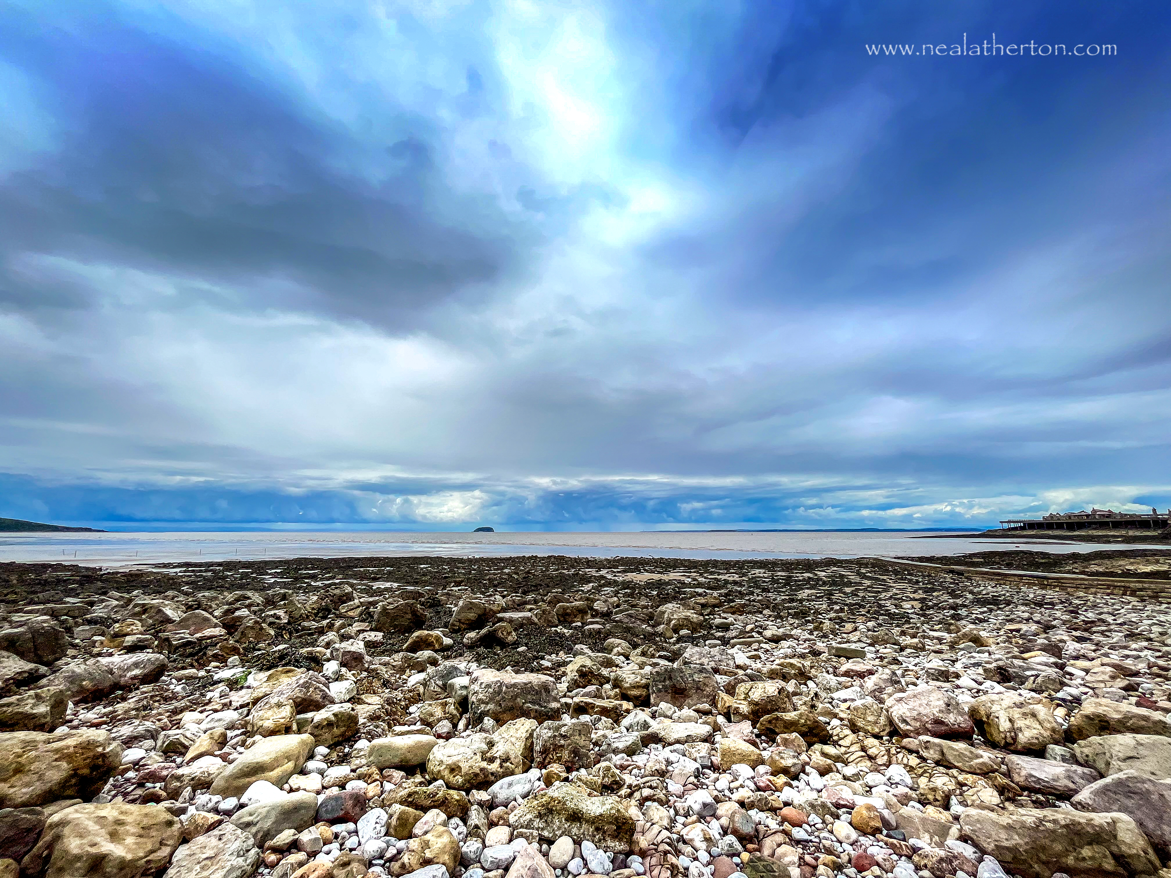 cobbles on the seashore with steep holm island in the distance and brean down on the left with Boirnbeck pier on the right