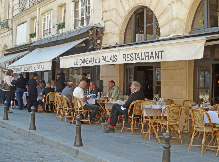 table and chairs on restaurant terrace with people eating under canopy