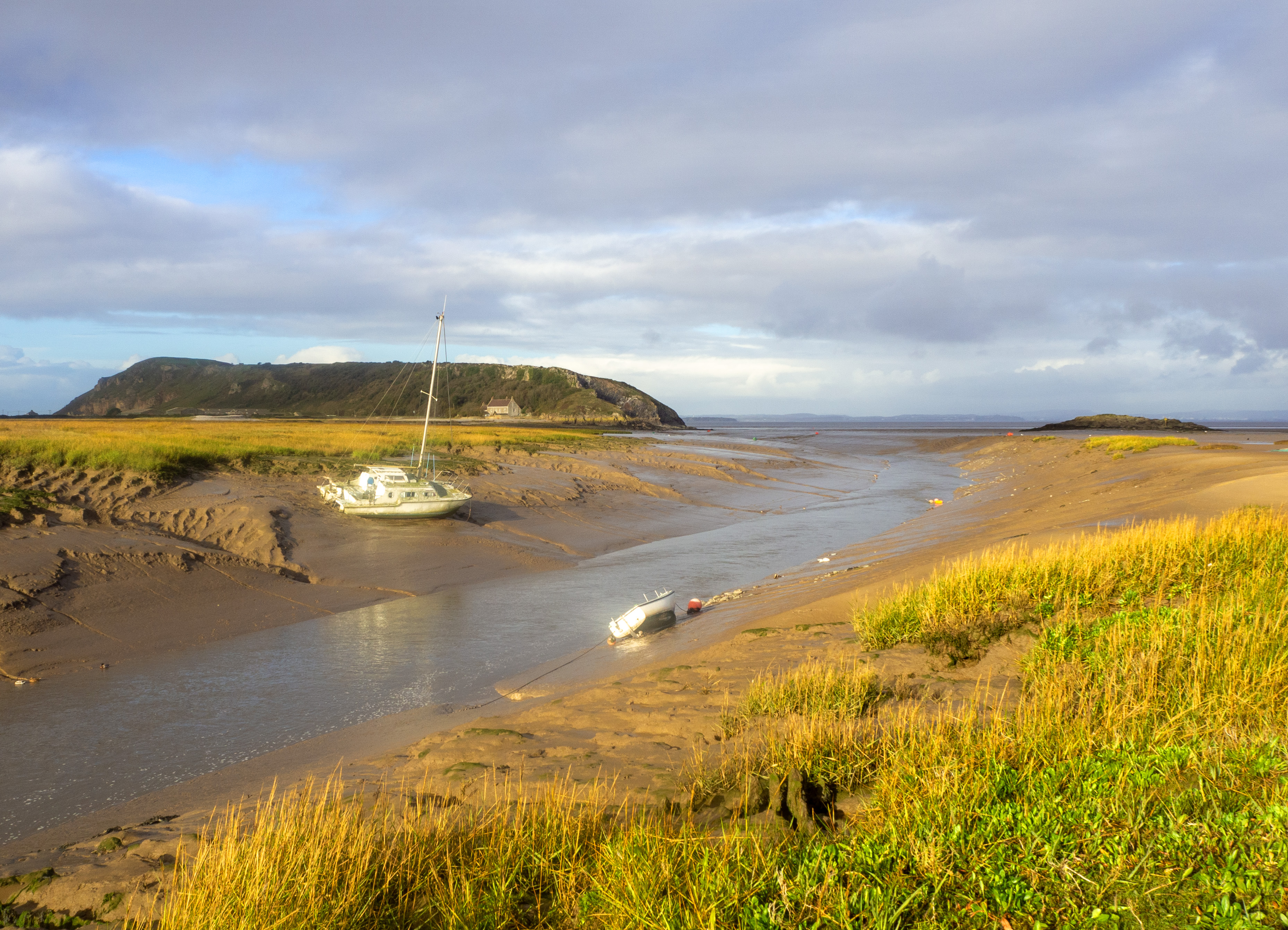 boats at low tide in estuary with autum colour and hill and sea