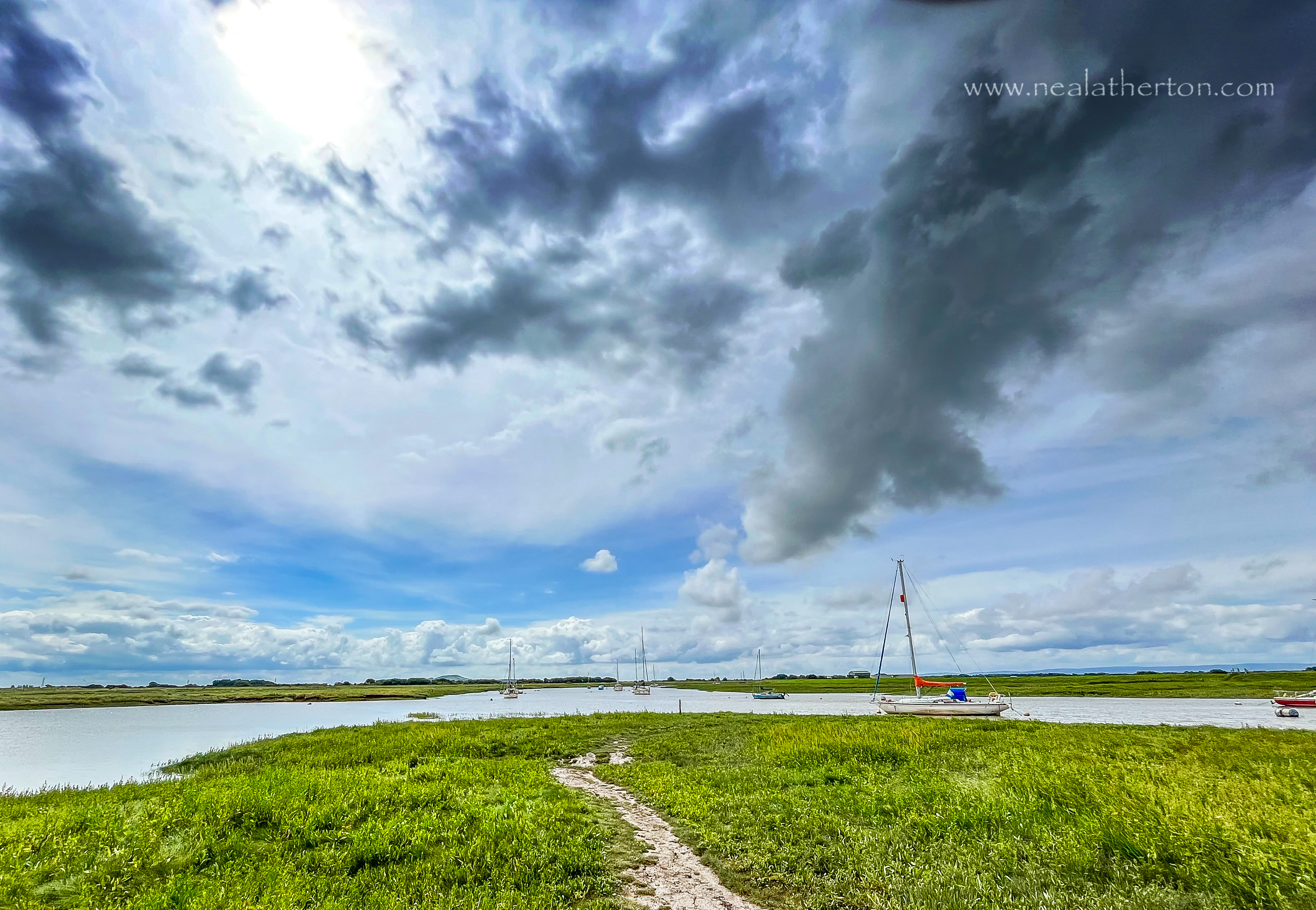 Tavhts in high tide river bend with grassy bank and unsettled sky