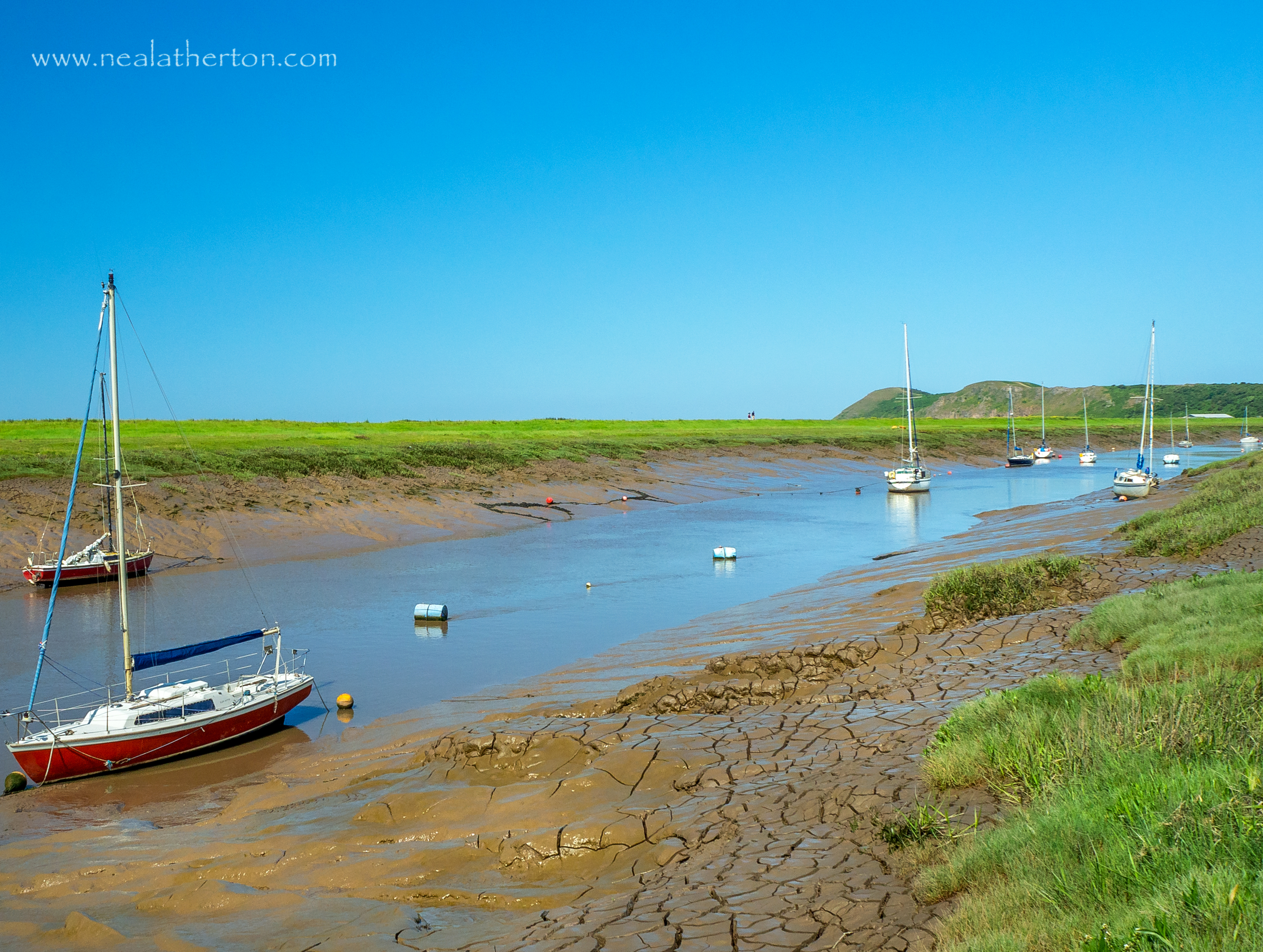 Several yachts and boats in the low tide mud with grassy banks and Brean Down with blue sky