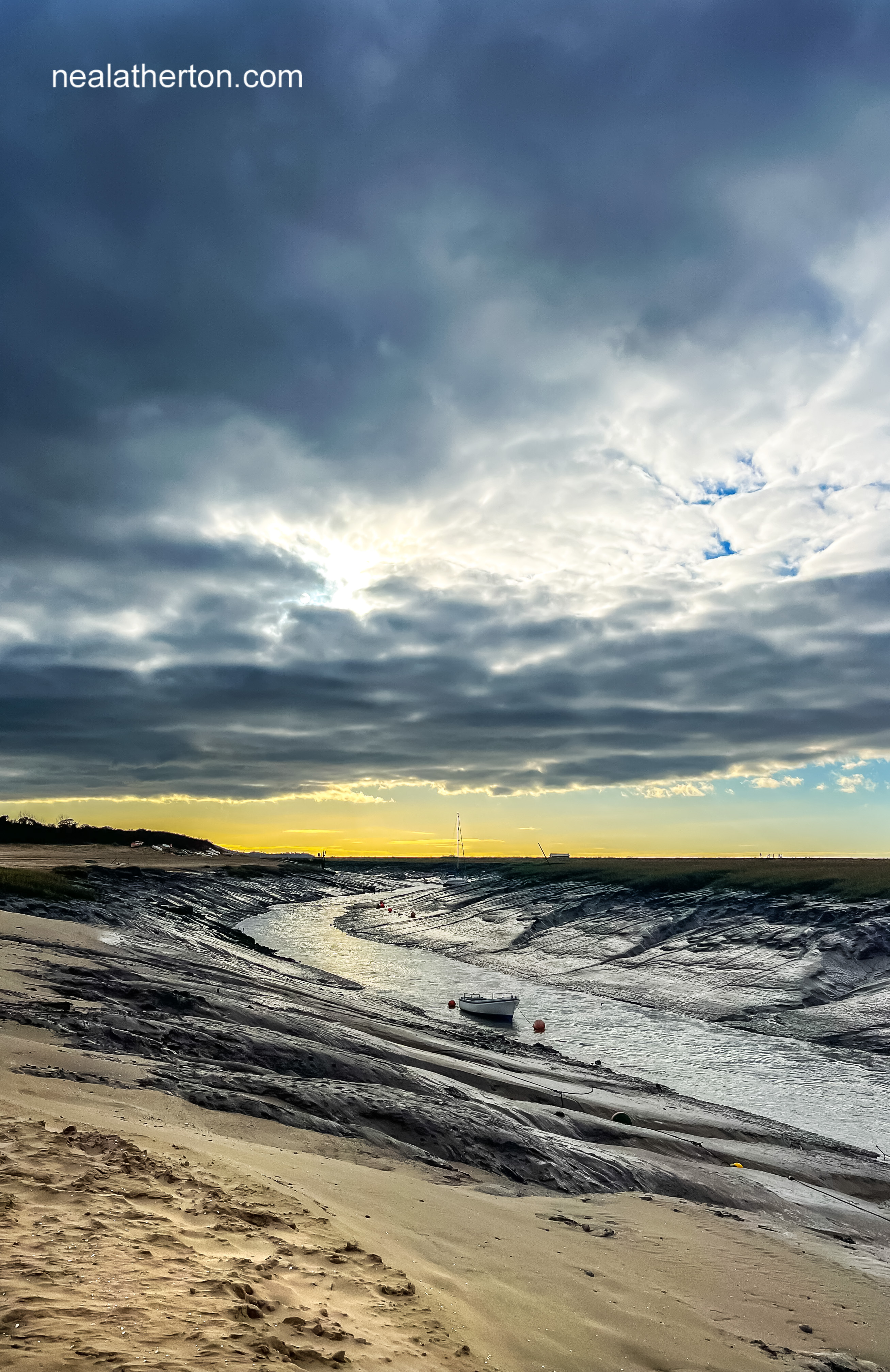 Pale sun breaks through the cloud over the estuary with yachts and boats at low tide
