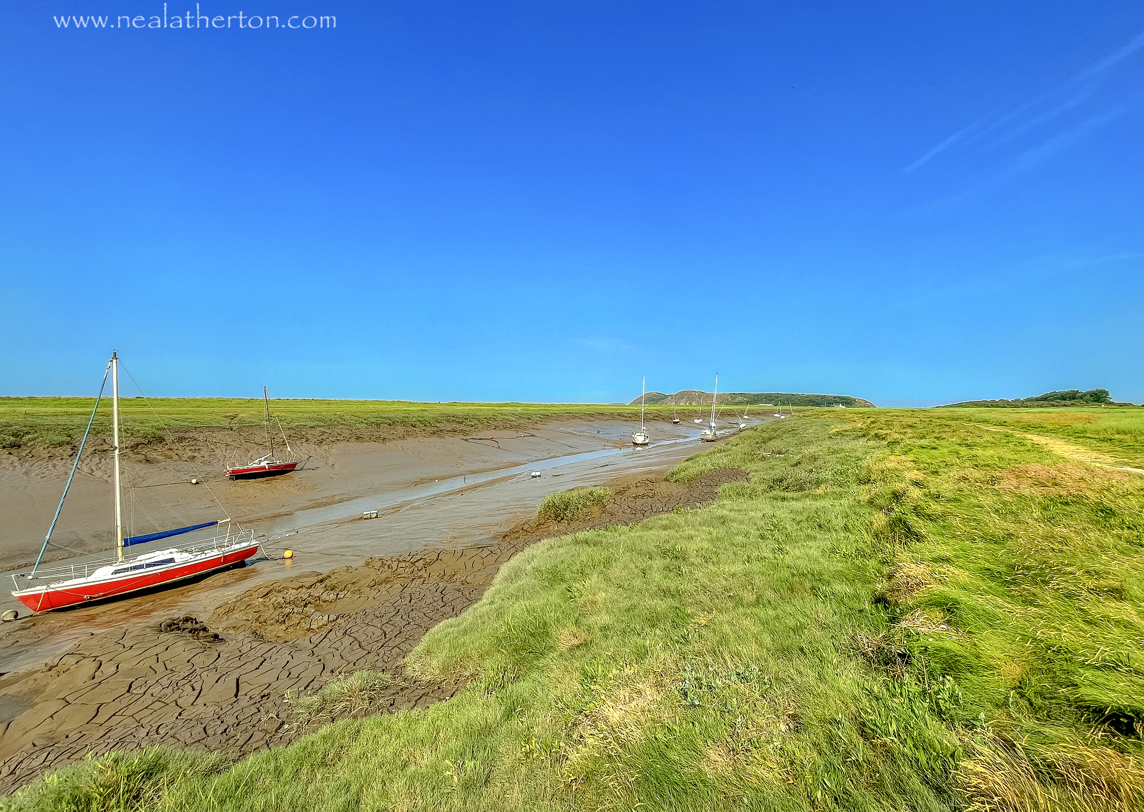 Yachts marooned at low tide in silt on a river with grassy banks and a deep blue sky
