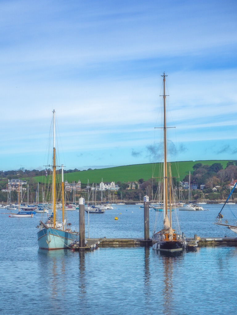two yachts in harbour with boats on estuary and hill with green fields and blue sky