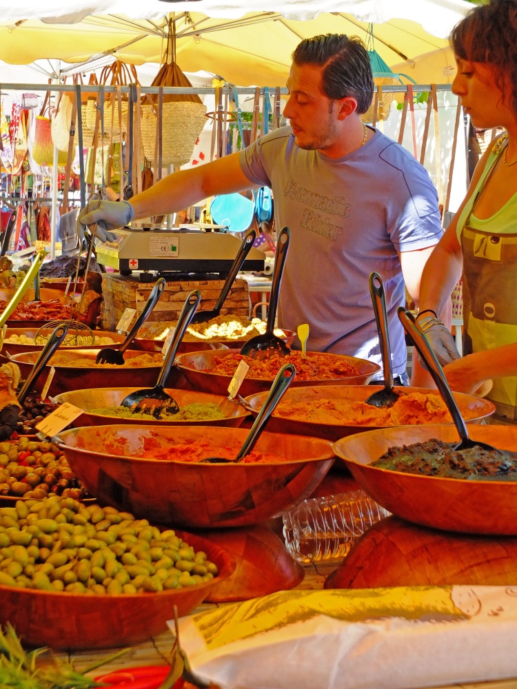 olives in dishes on market stall with man and lady