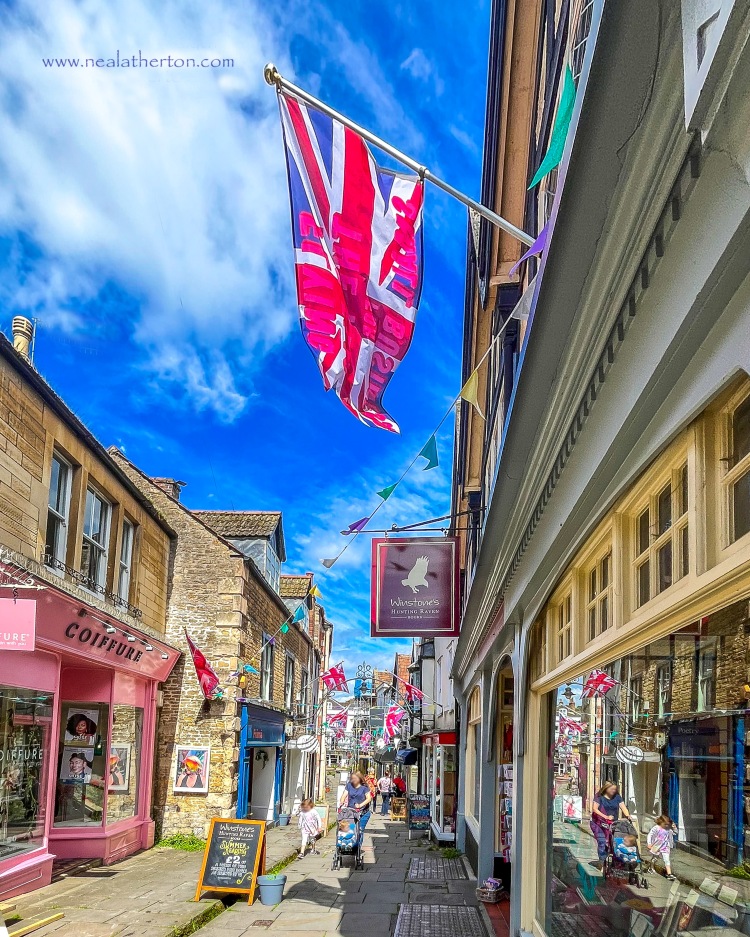 flag flying from old shop with other shops and signs on paved old street with deep blue sky