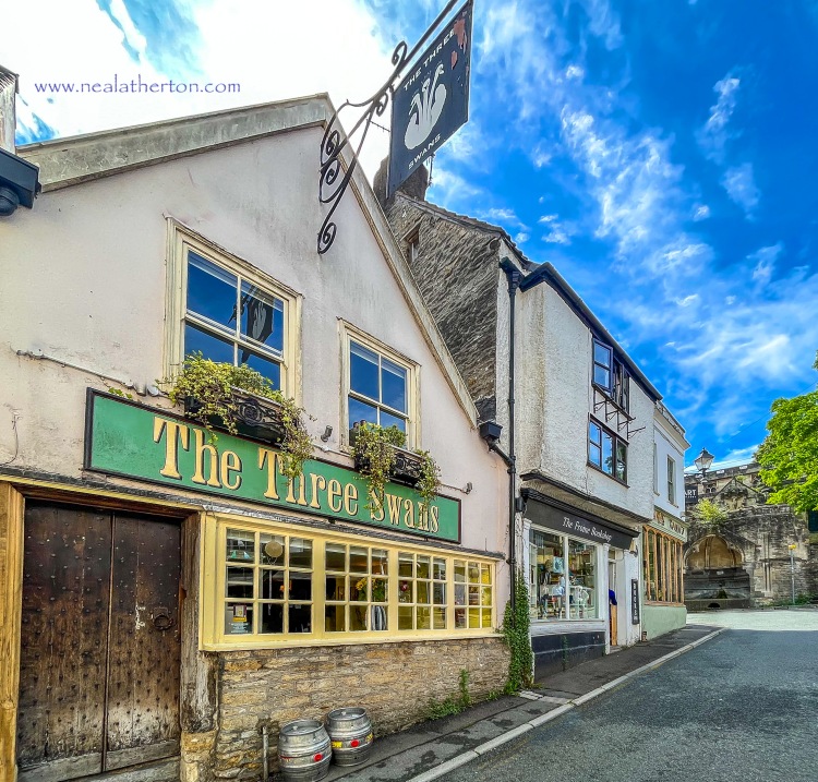 pub with sign and barrells with two shops and church under blue sky