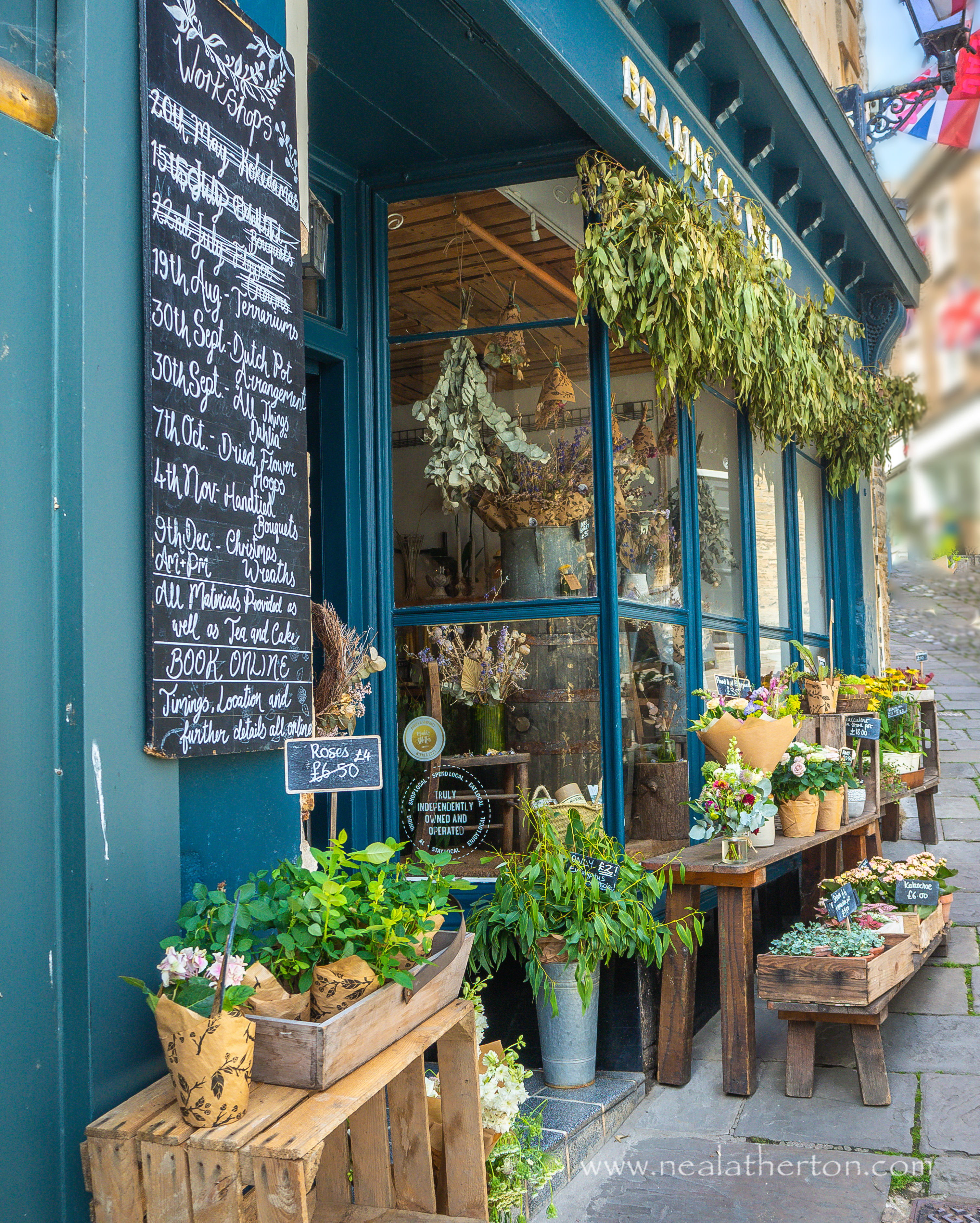 flower and plant display in front of shop on paved street with flags and sign