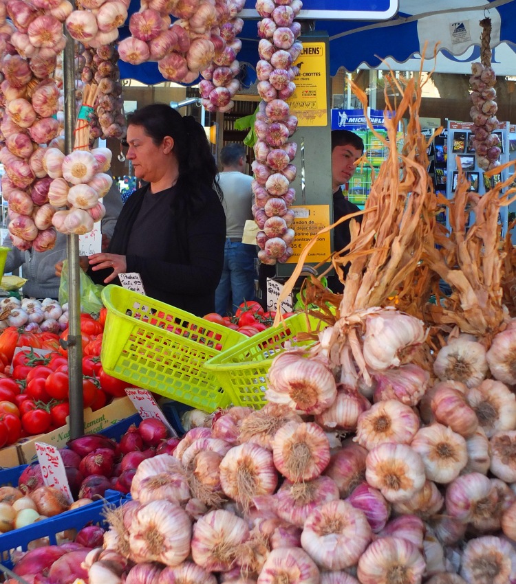 garlic bulbs on market stall with tomatoes and baskets with lady