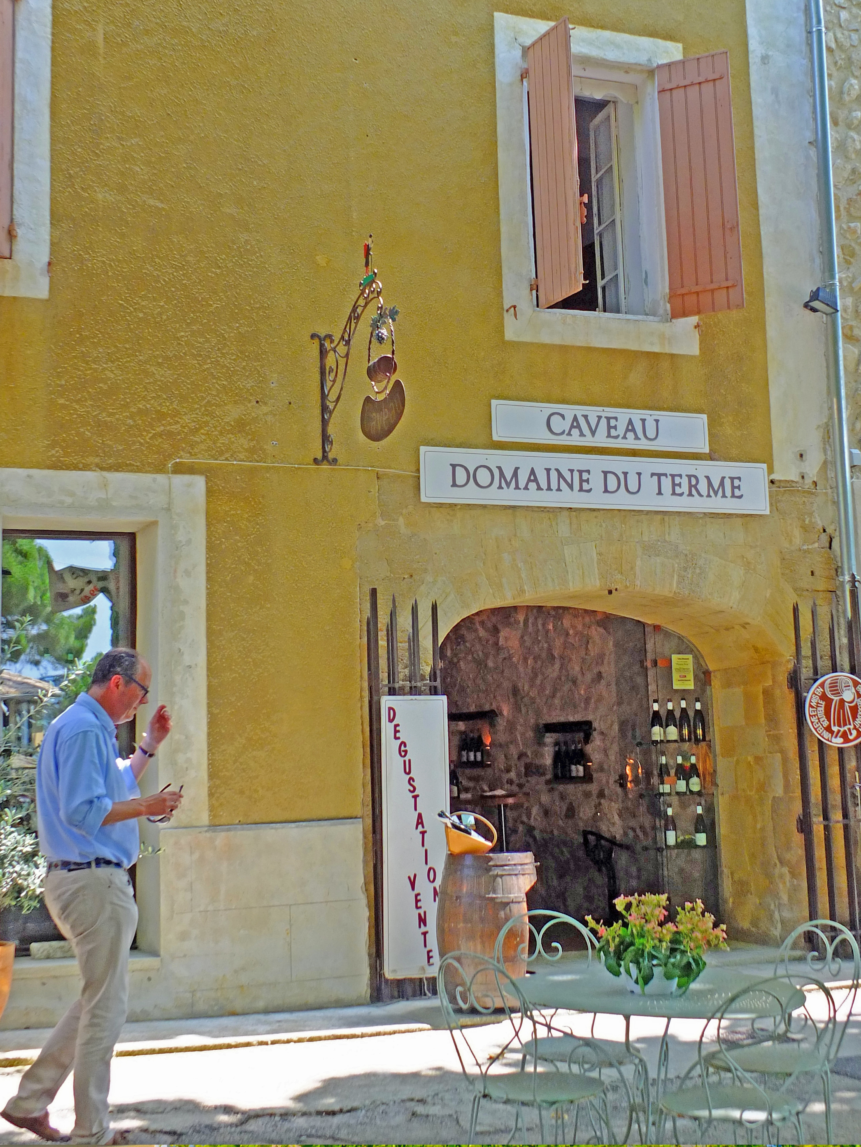 Man in front of wine cave with table and chairs and wine bottles