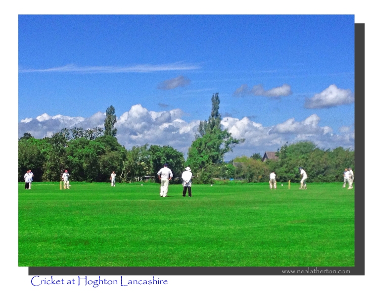 game of cricket on green pitch with white dressed men and trees with blue sky