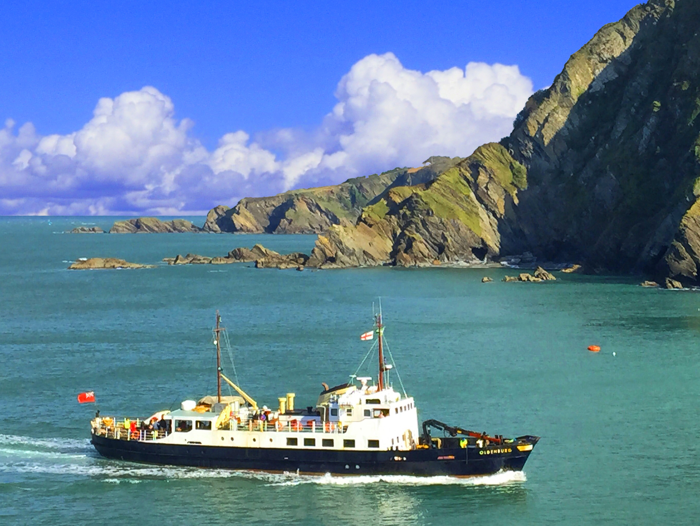 On sea a boat comes in to port with cliffs and blue sky with clouds