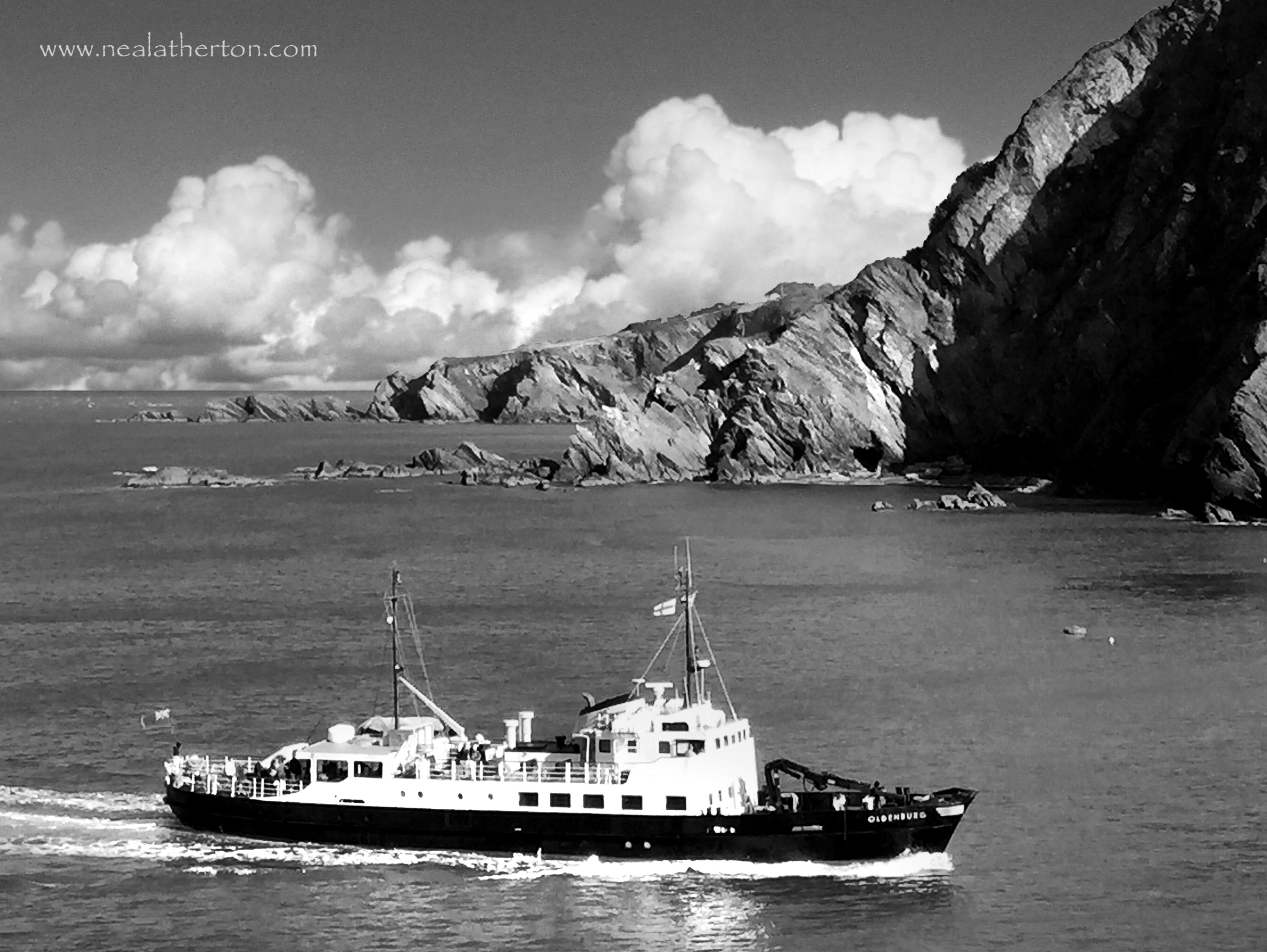 boat on sea with cliffs behind and white clouds in summer sky
