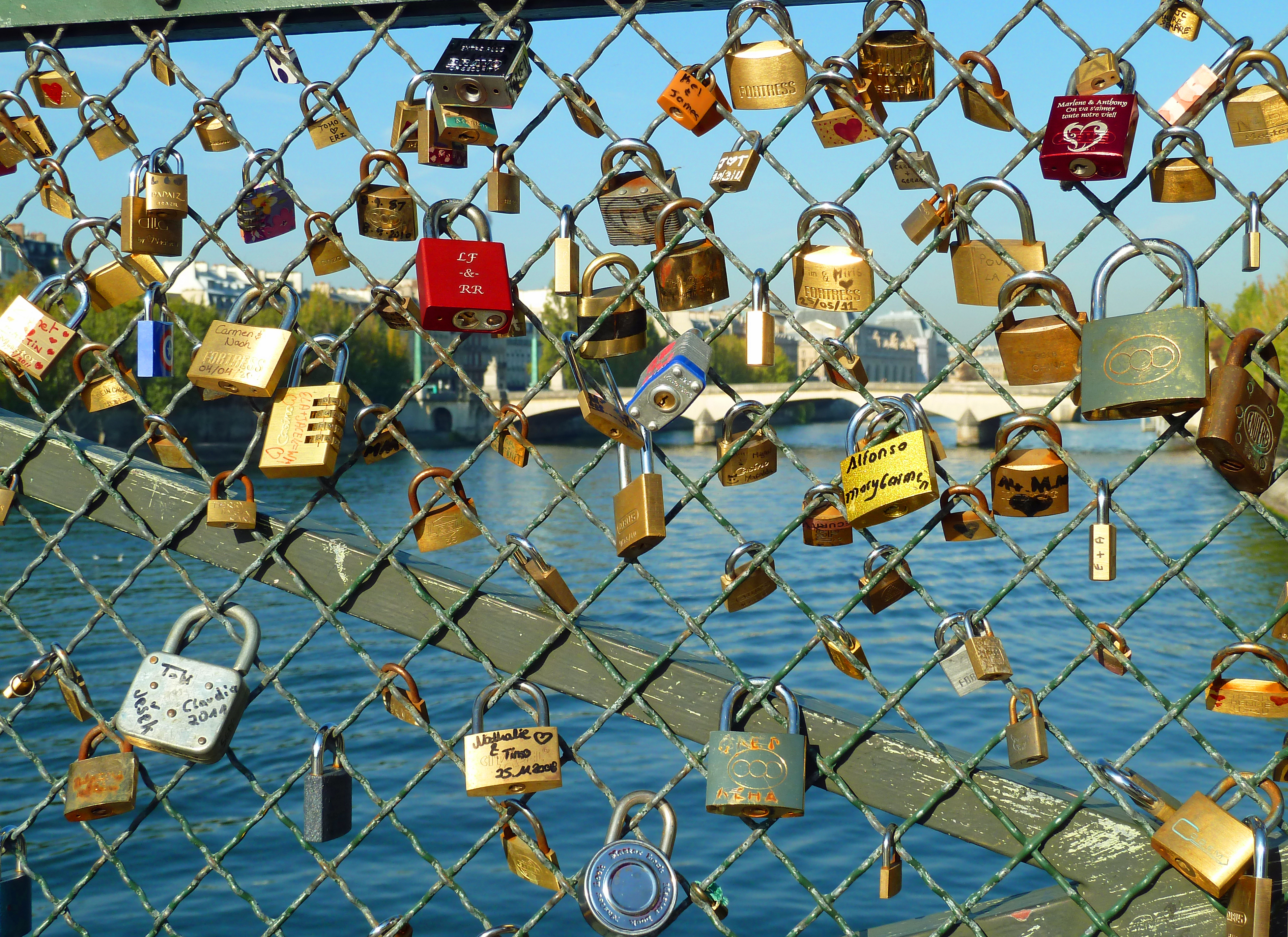 locks on wire railing on bridge over river with Paris in background