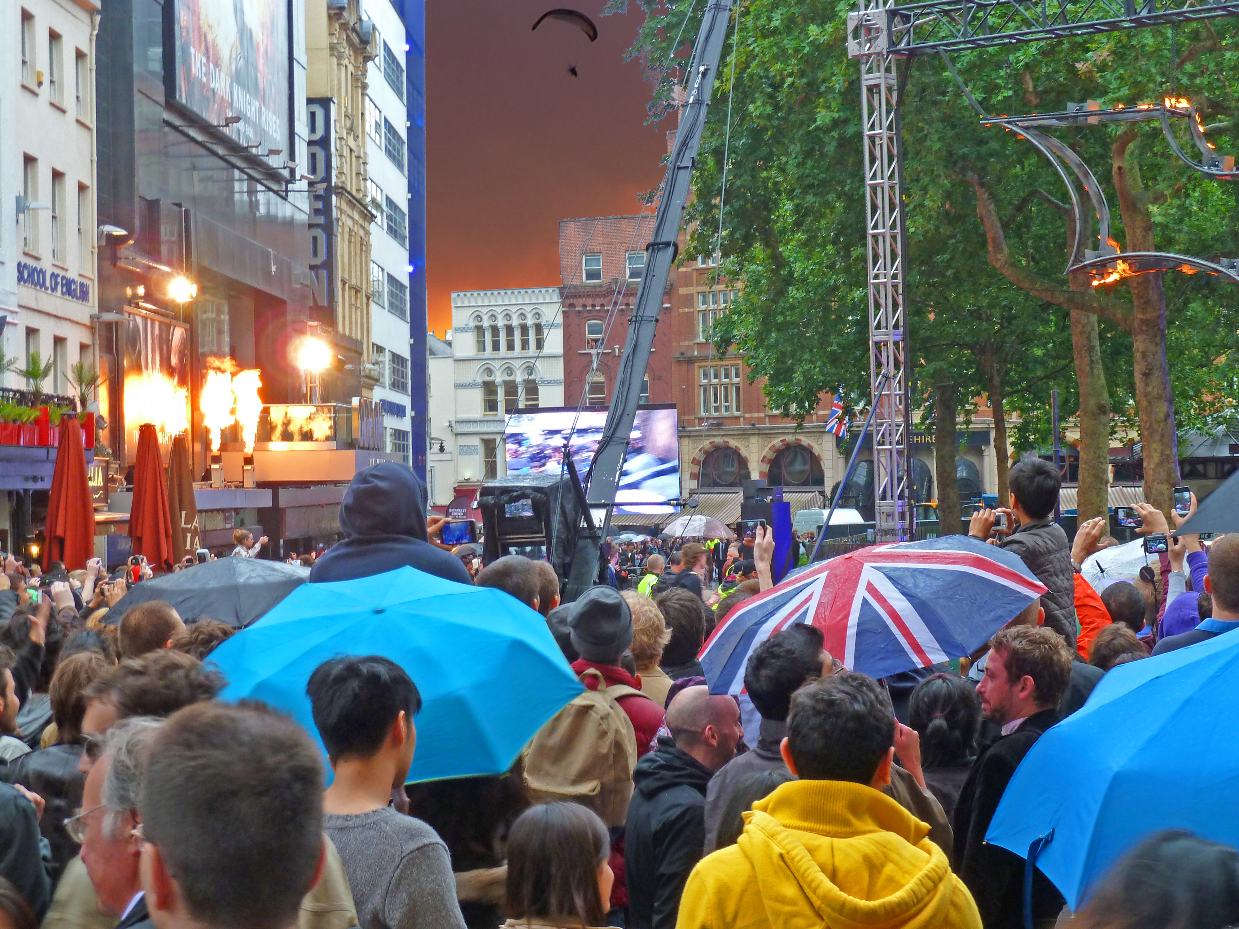 people with umbrellas in front of cinema in square with buildings